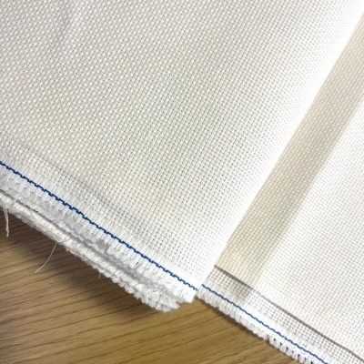 Tecido branco com textura quadriculada e costura azul sobre madeira clara