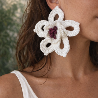 Brinco grande de flor em crochet branco com contas roxas ao centro, usado por mulher