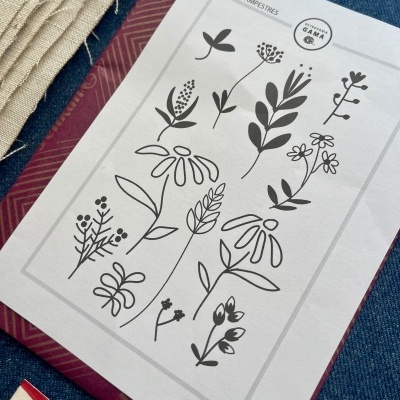 Desenhos a preto de flores em folha branca sobre livro e tecidos coloridos