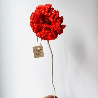 Flor artesanal em lã vermelha com etiqueta Handmade, haste bege, mão a segurar