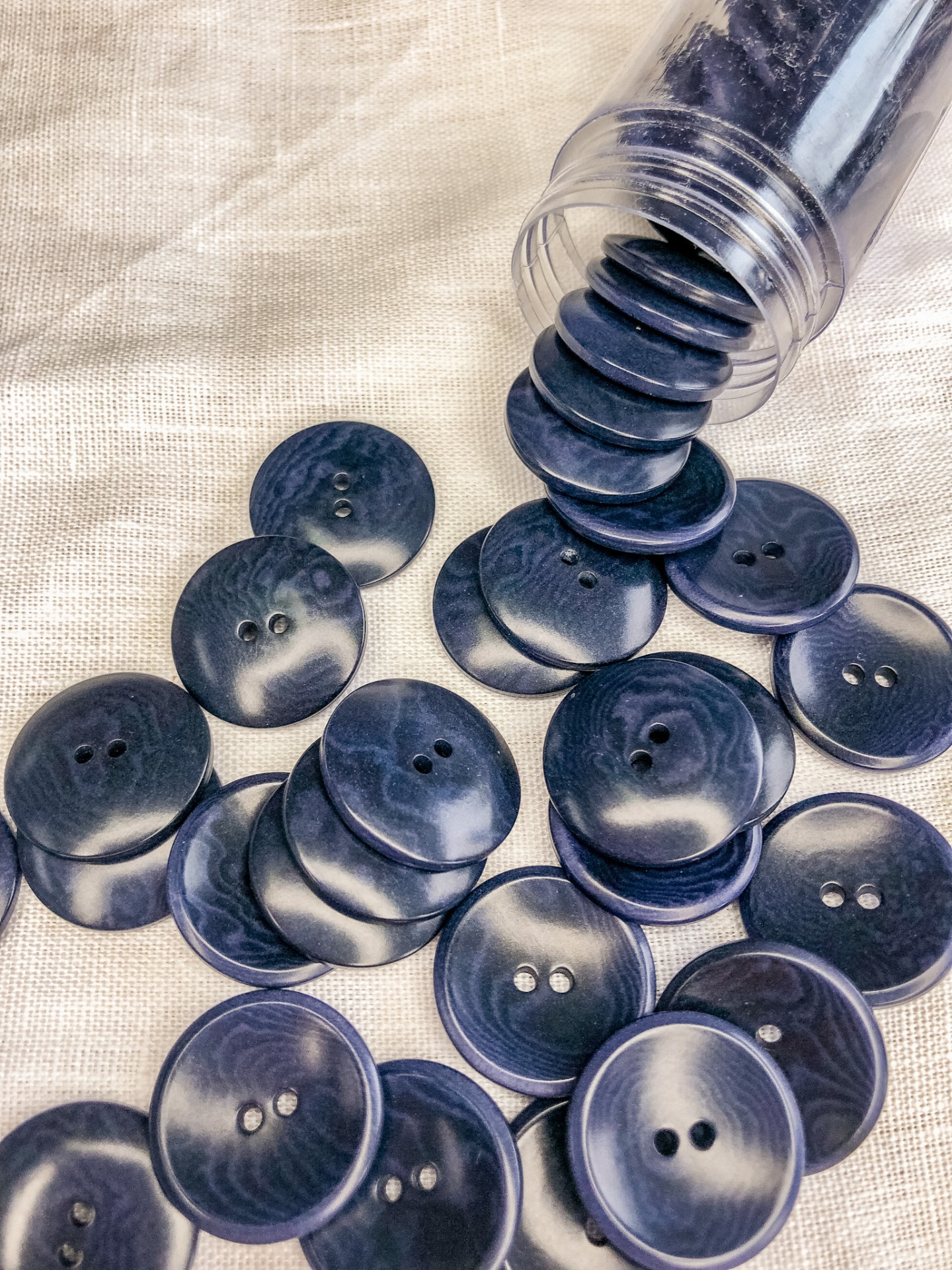 Botões azuis escuros marmoreados com dois orifícios sobre tecido claro e frasco transparente