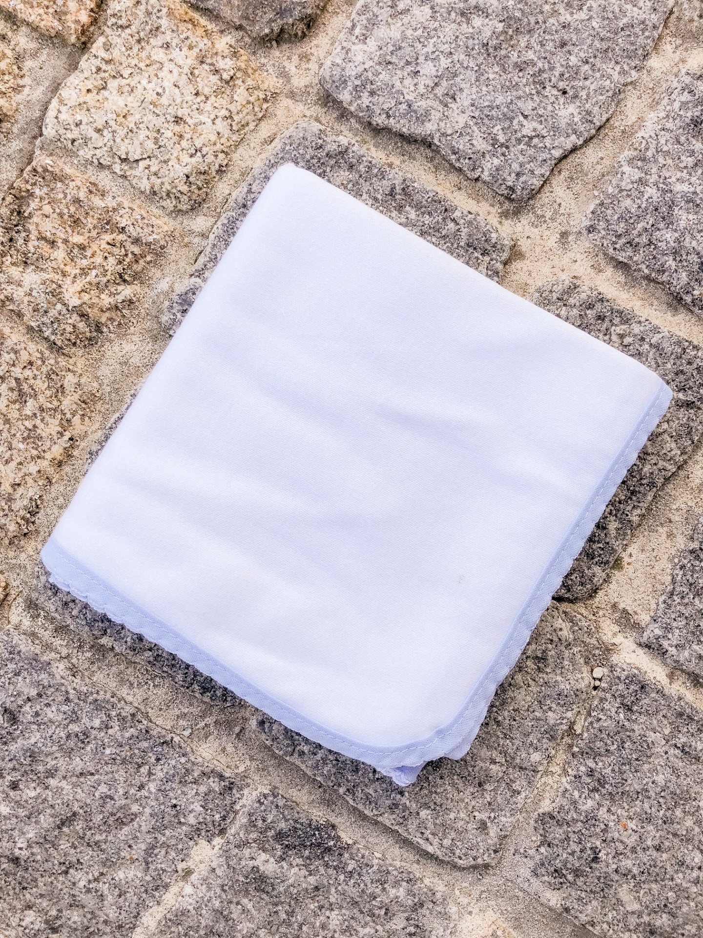 Toalha branca com borda azul claro sobre chão de pedras cinza