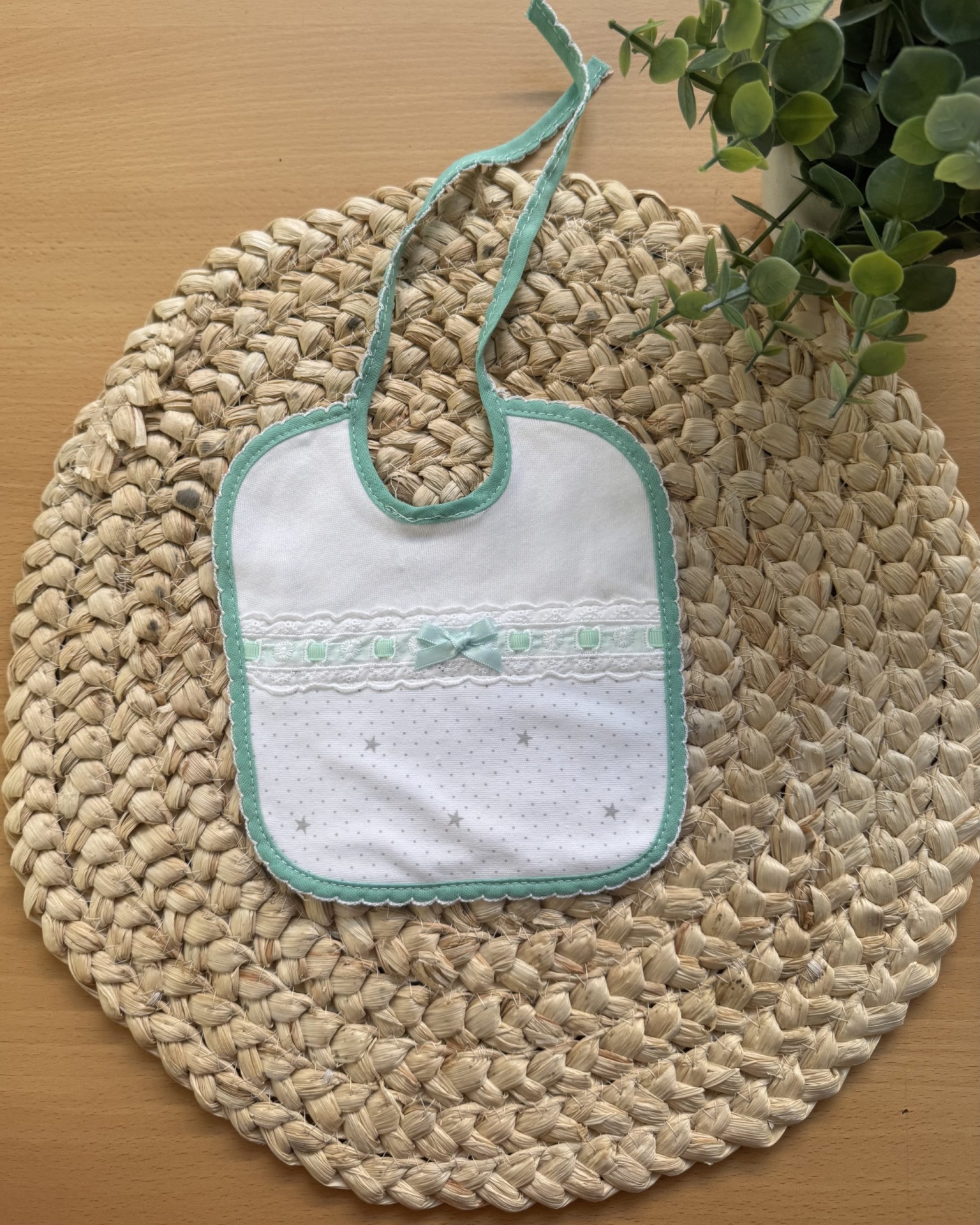 Babete branco com bordas verdes e detalhes em renda e laço sobre base redonda trançada