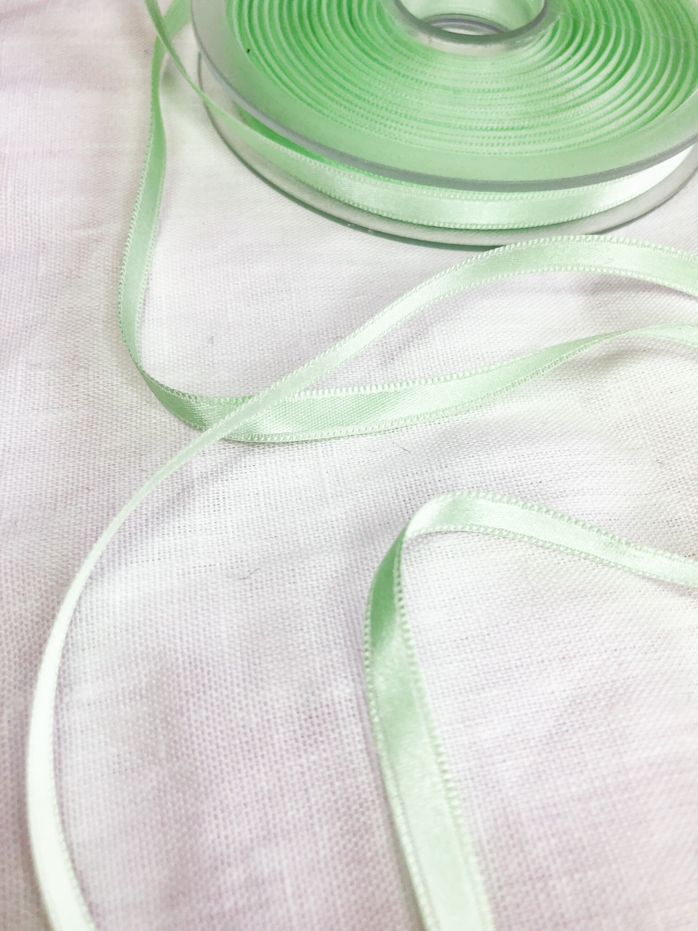 Fita de cetim verde claro em rolo sobre tecido branco