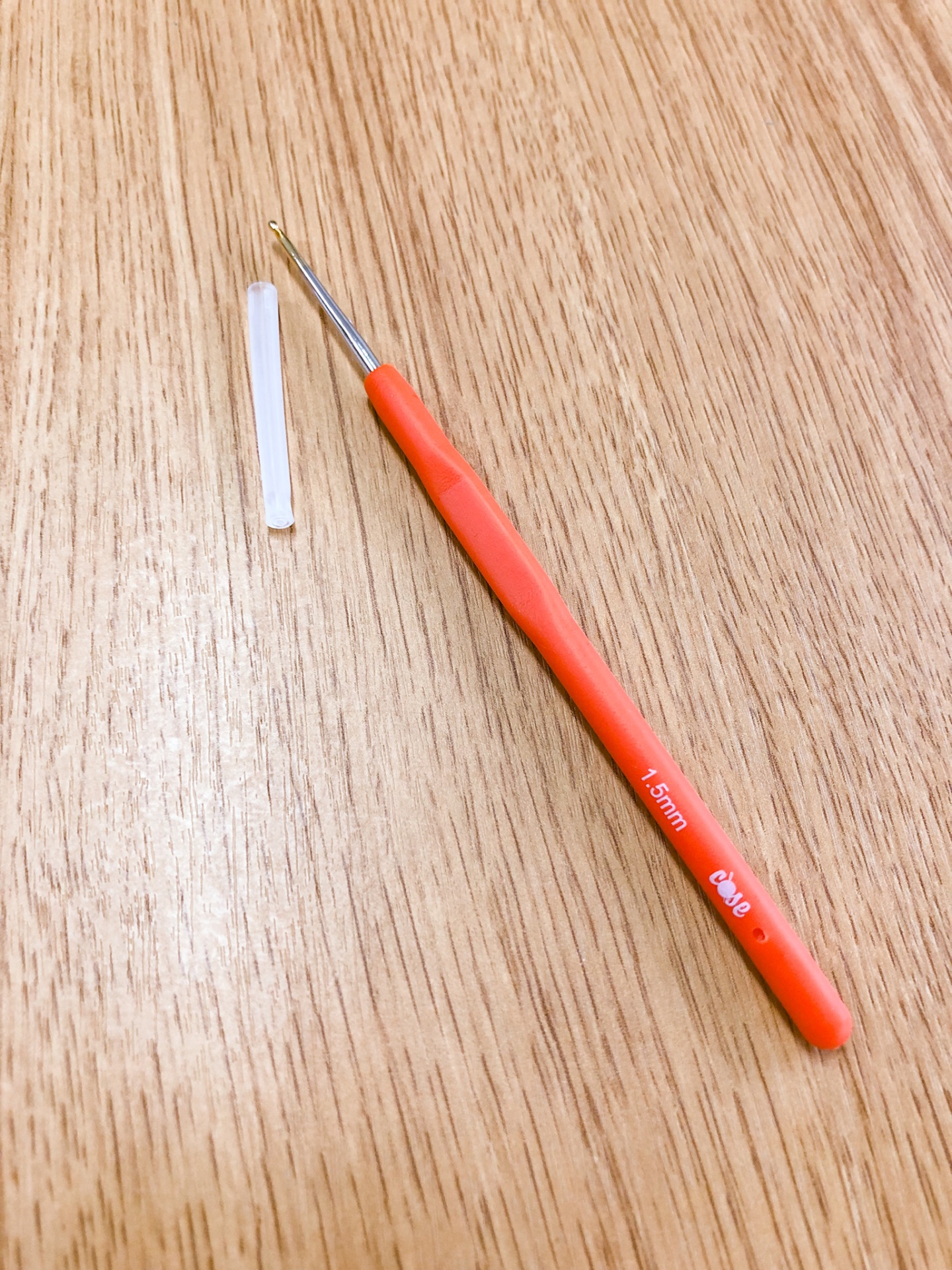 Agulha de crochet com cabo laranja e protetor branco sobre mesa de madeira