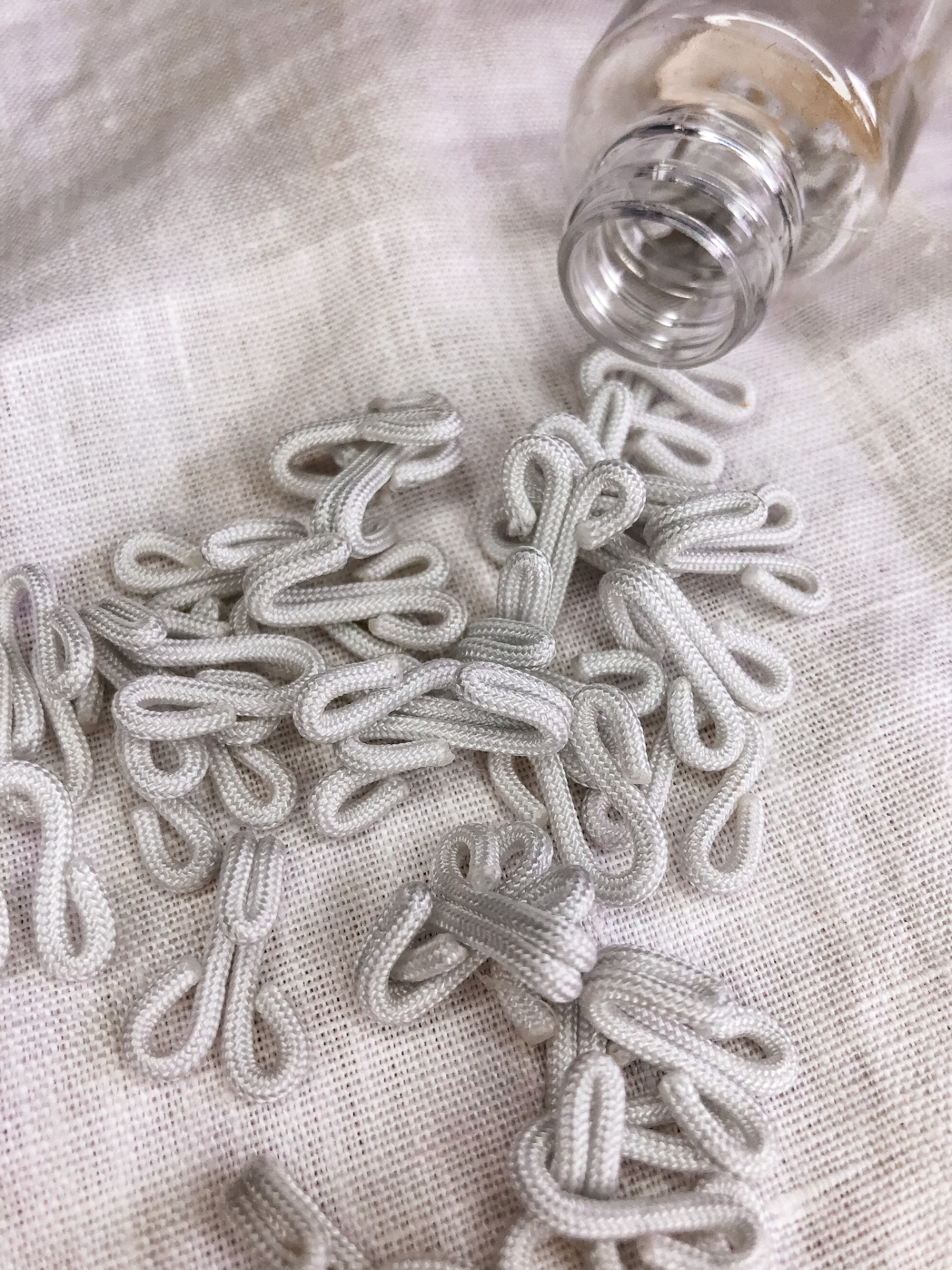 Botões de nó tubulares brancos em tecido sobre pano bege e frasco de vidro