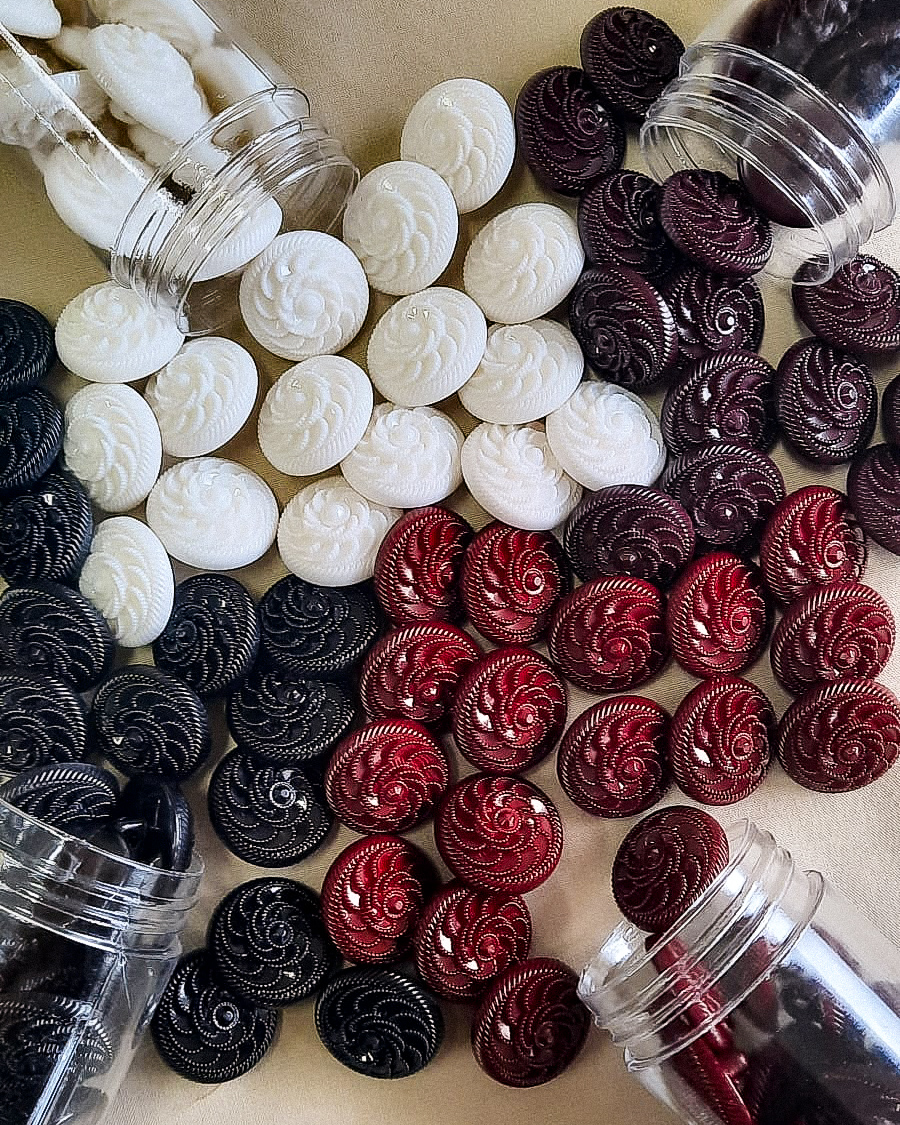 Botões redondos coloridos com padrão espiral em recipientes transparentes sobre superfície clara