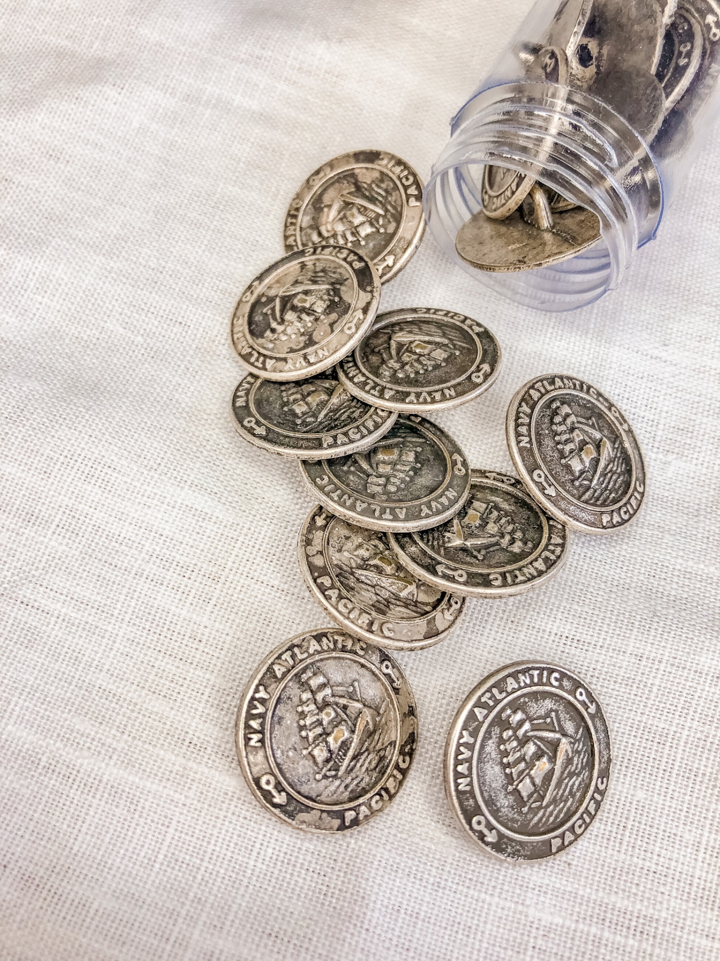 Moedas metálicas prateadas com texto NAVY ATLANTIC PACIFIC sobre tecido branco