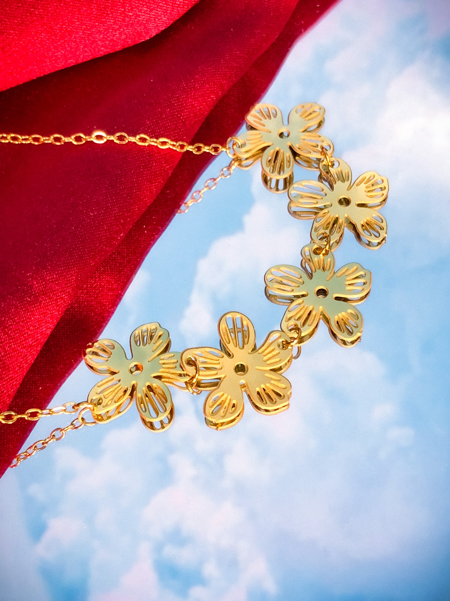 Colar dourado com cinco flores decorativas sobre fundo vermelho e céu azul