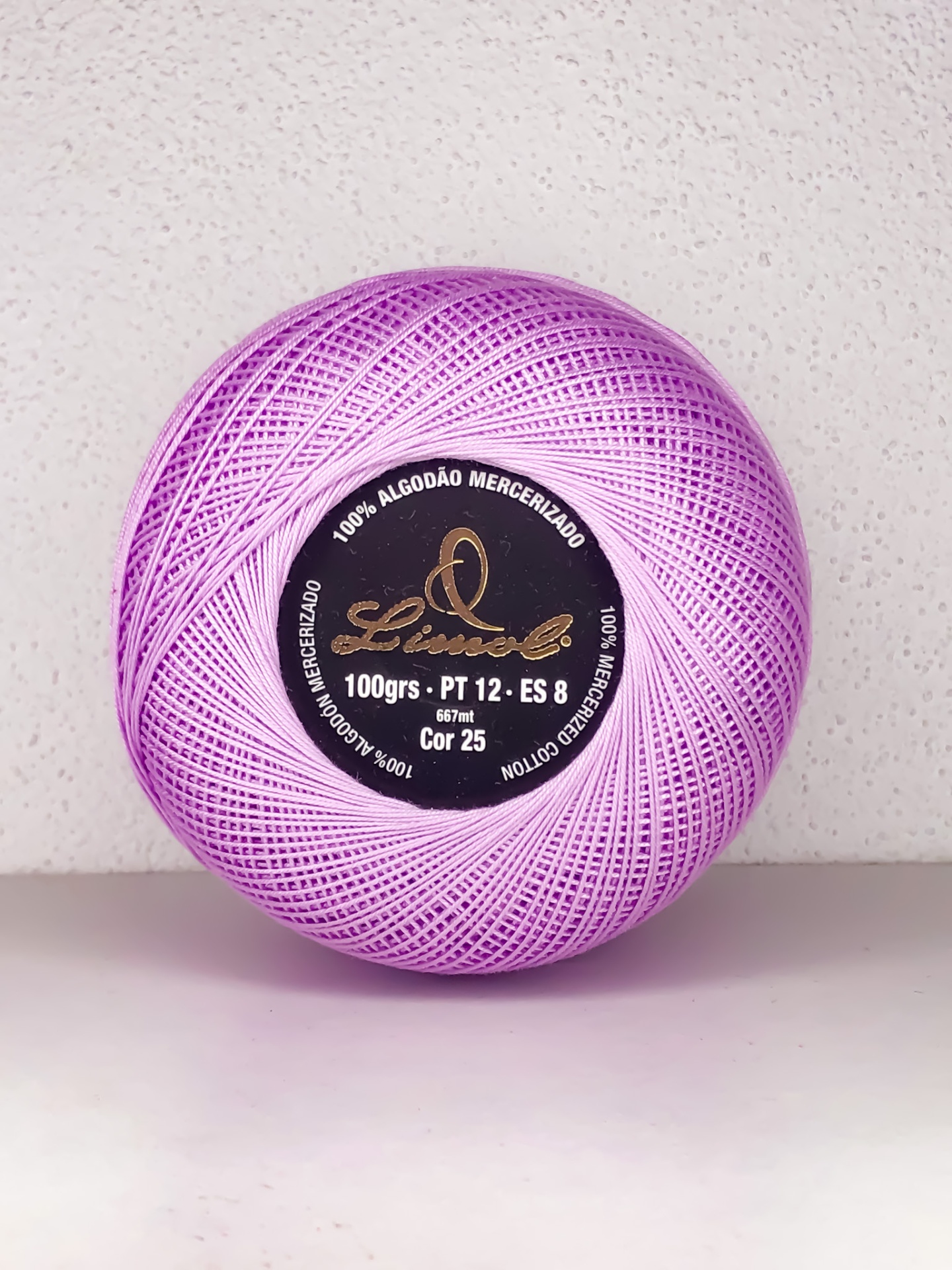 Rolo de linha de algodão mercerizado lilás com etiqueta preta e dourada sobre superfície branca