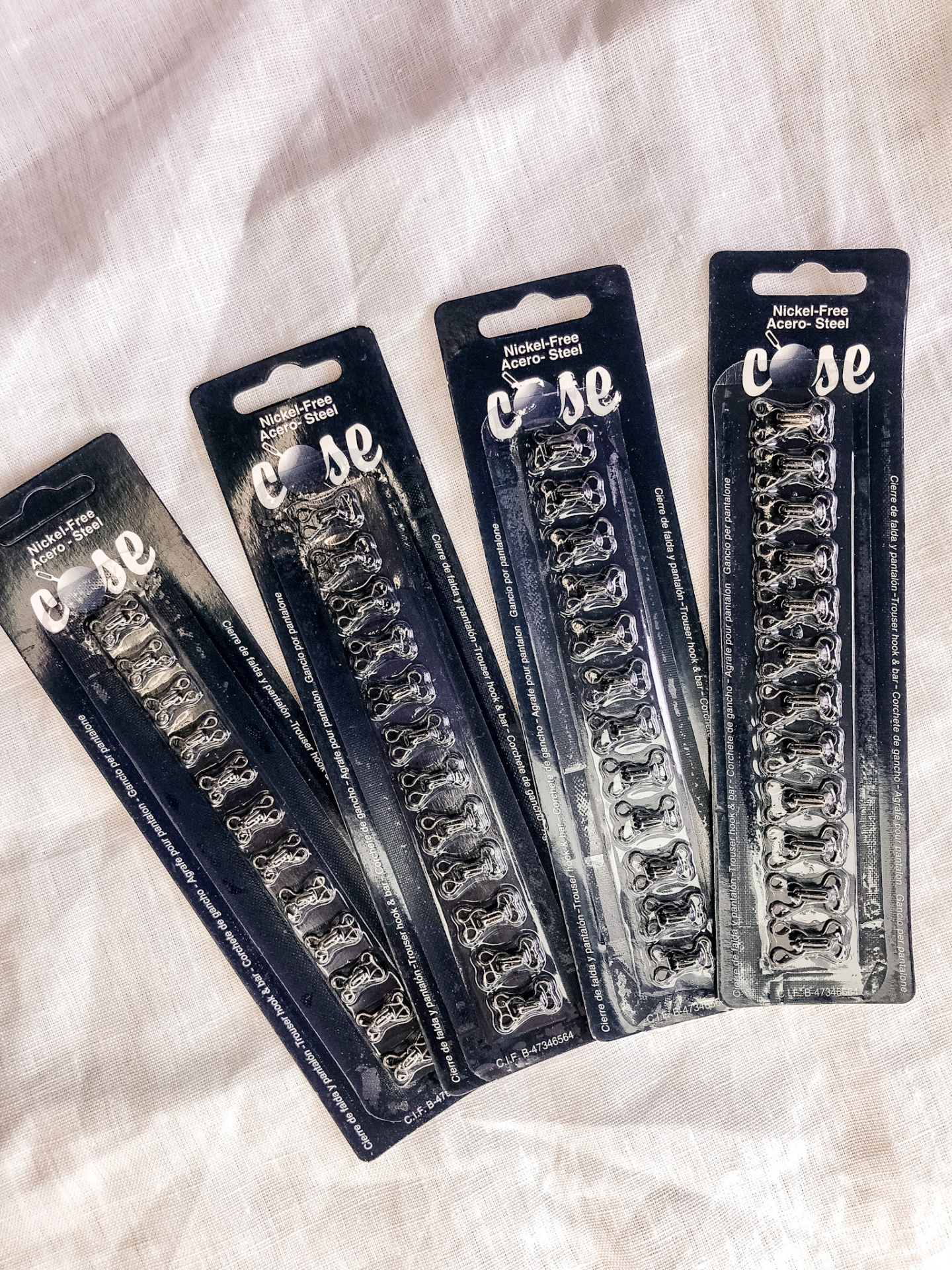 Pacotes de ganchos metálicos em fundo azul escuro sobre tecido branco