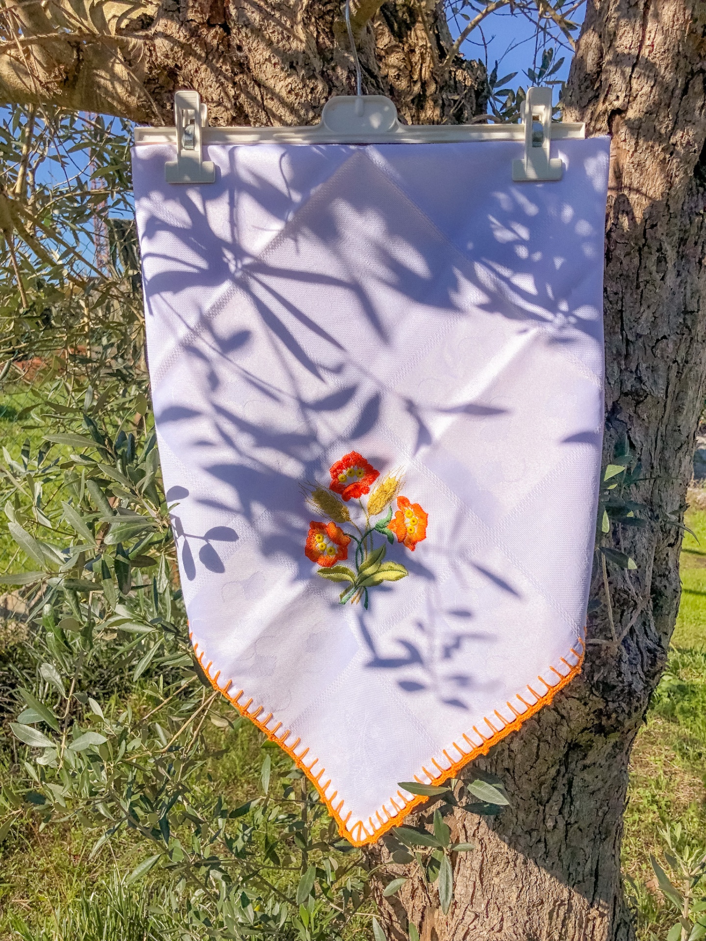 Pano branco bordado com flores coloridas pendurado numa árvore
