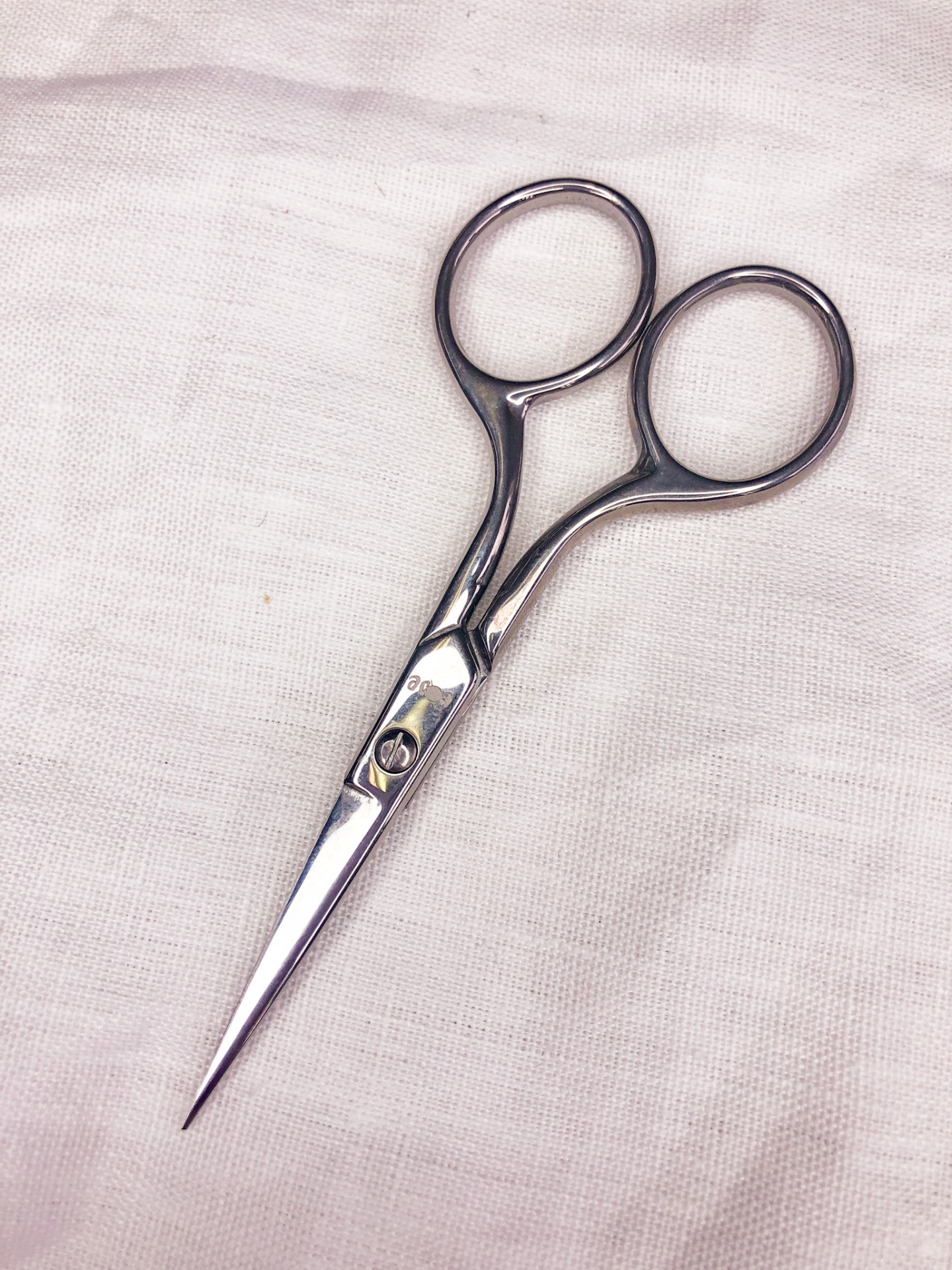 Tesoura pequena prateada sobre tecido branco