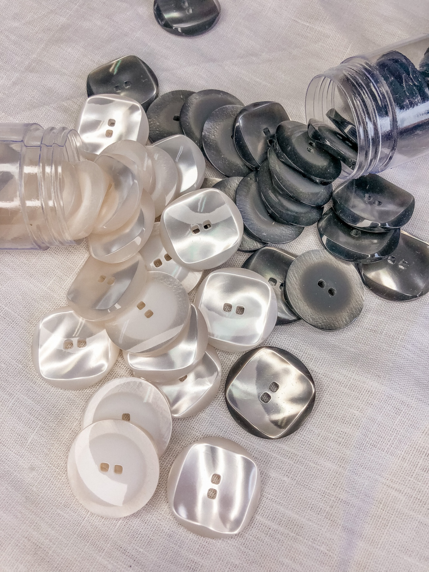 Botões quadrados perolados branco e cinza com dois furos sobre tecido branco