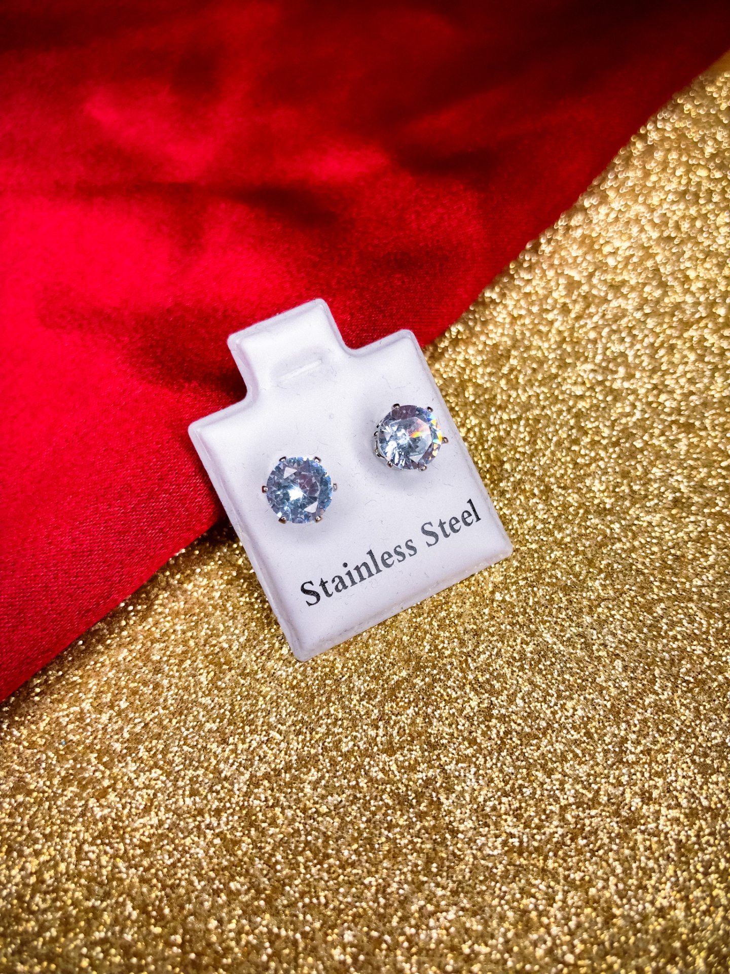 Brincos de aço inoxidável com pedras redondas em estojo branco sobre fundo dourado e vermelho