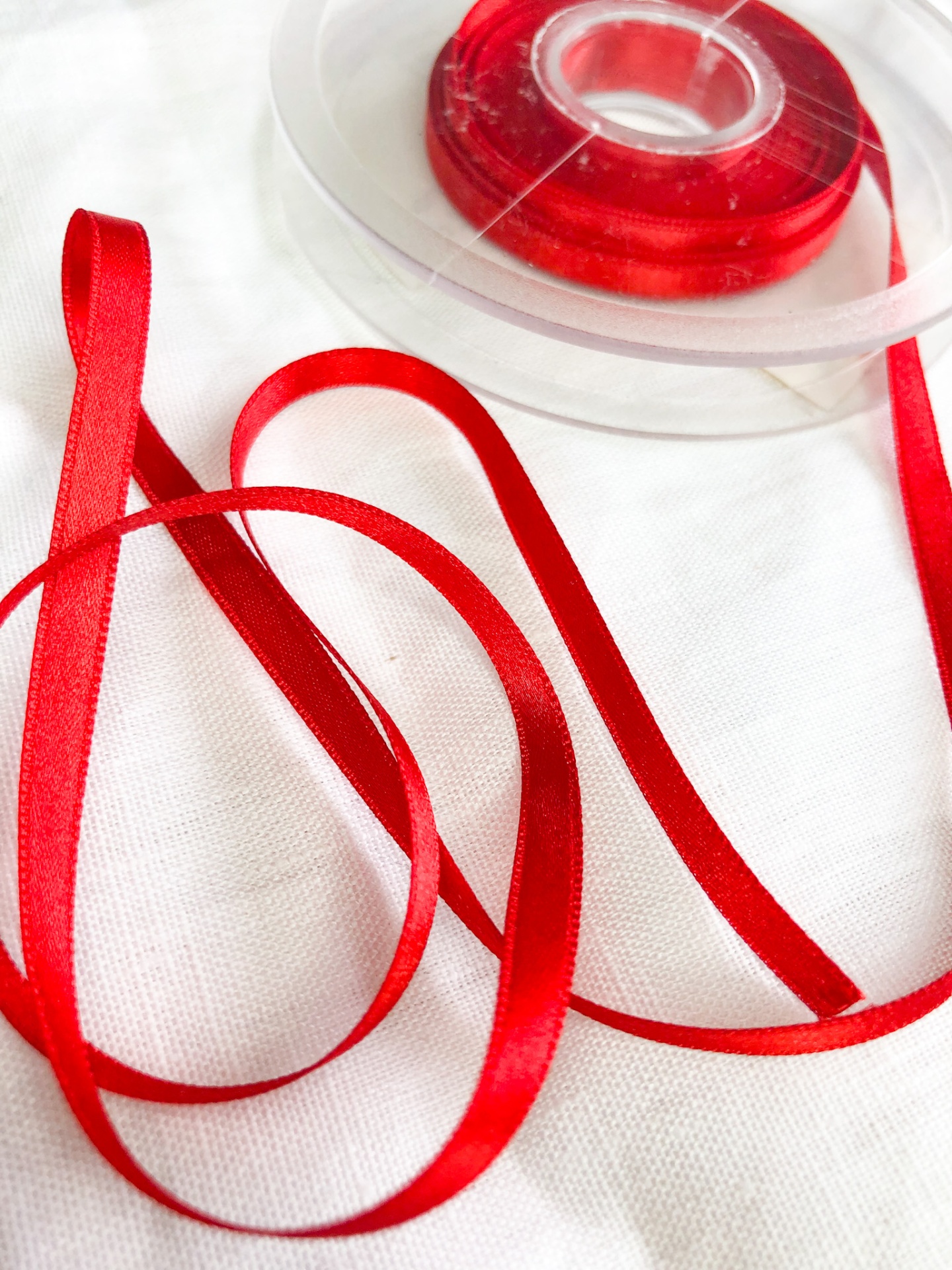 Fita de cetim vermelha fina em bobina plástica transparente sobre tecido branco