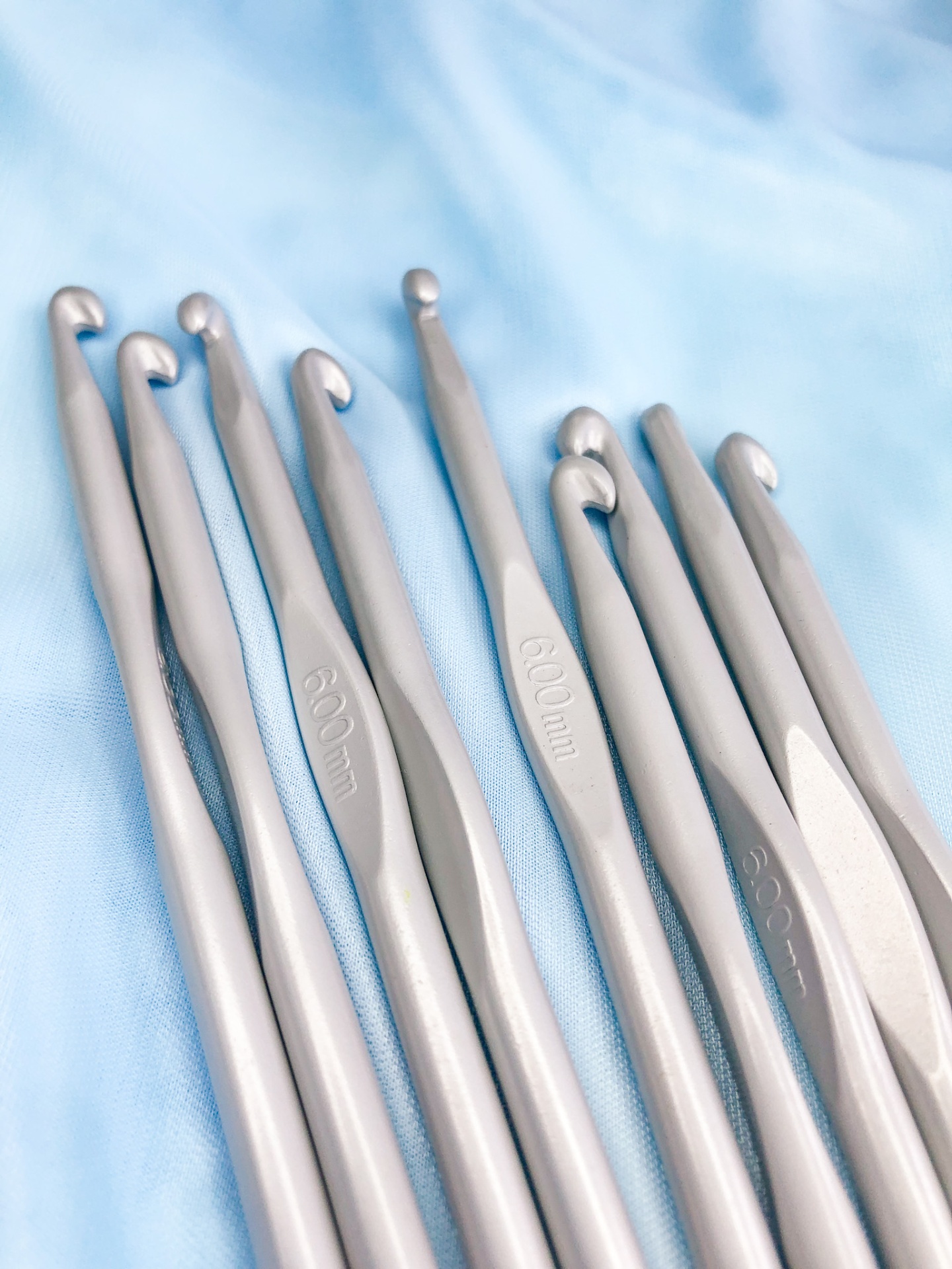 Agulhas de crochet prateadas com tamanhos gravados sobre tecido azul