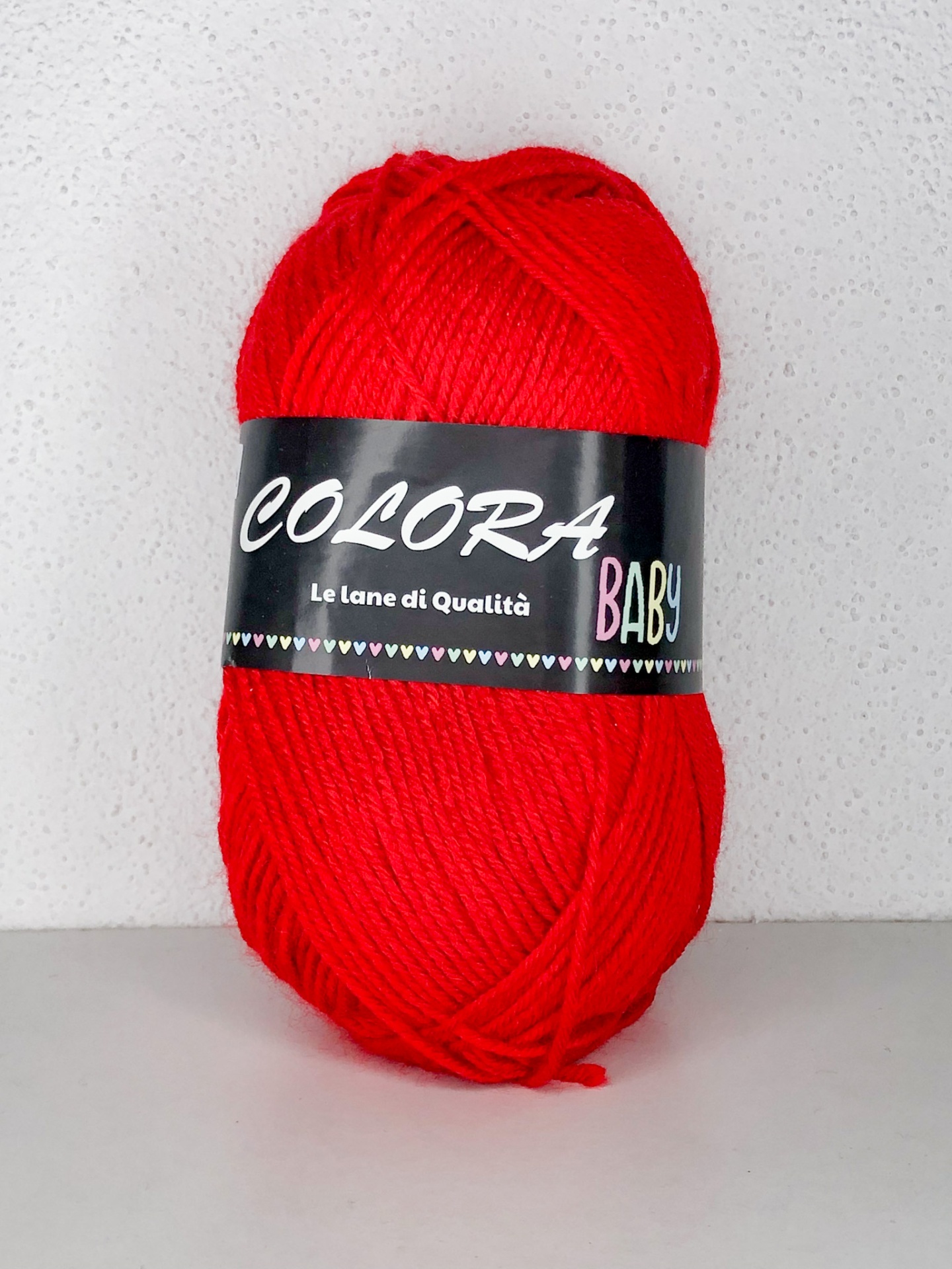 Novelo de lã vermelho com etiqueta preta 'COLORA BABY Le lane di Qualità'
