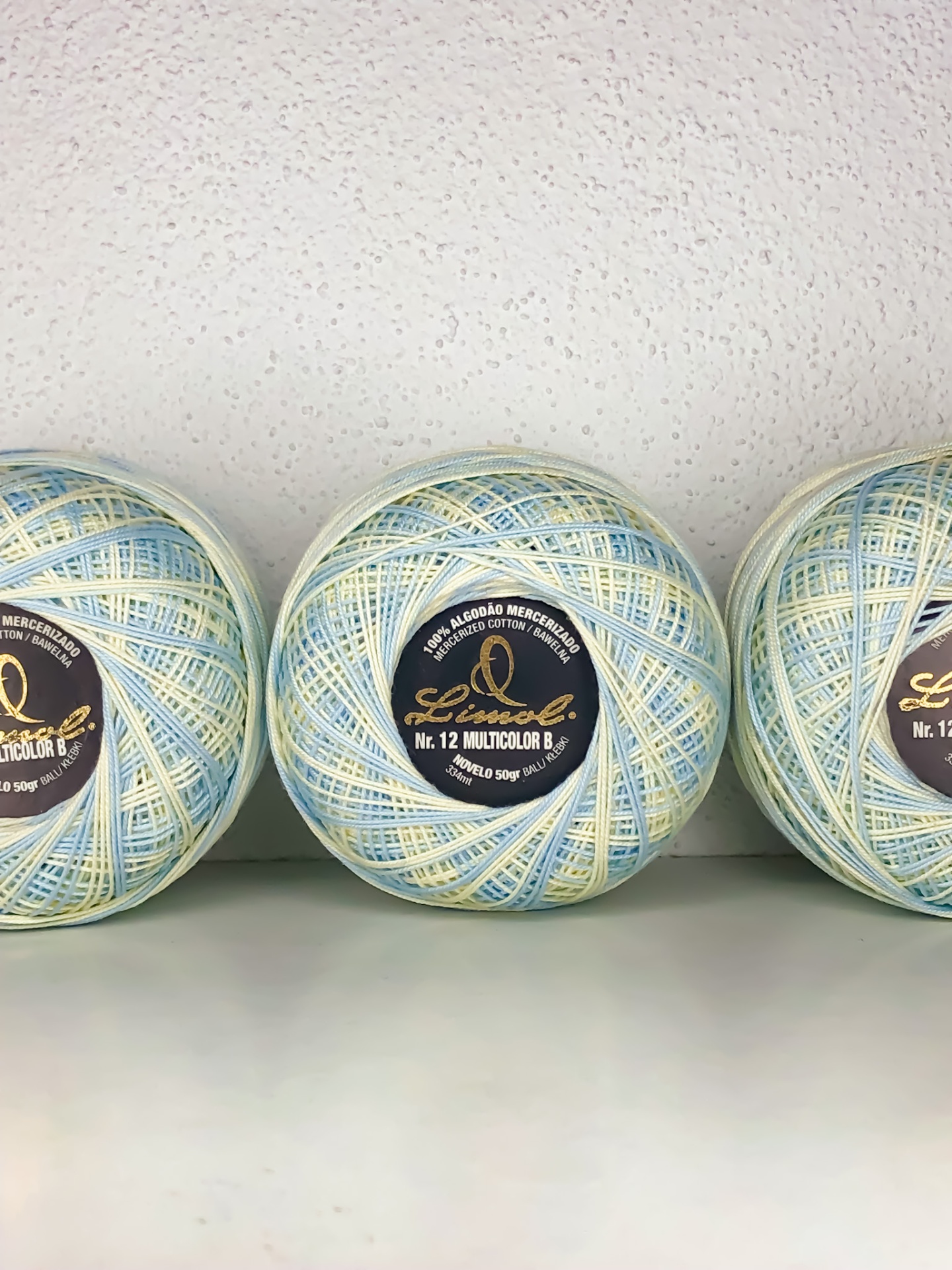 Três novelos de linha multicolor azul, branco e amarelo com rótulos pretos sobre superfície branca