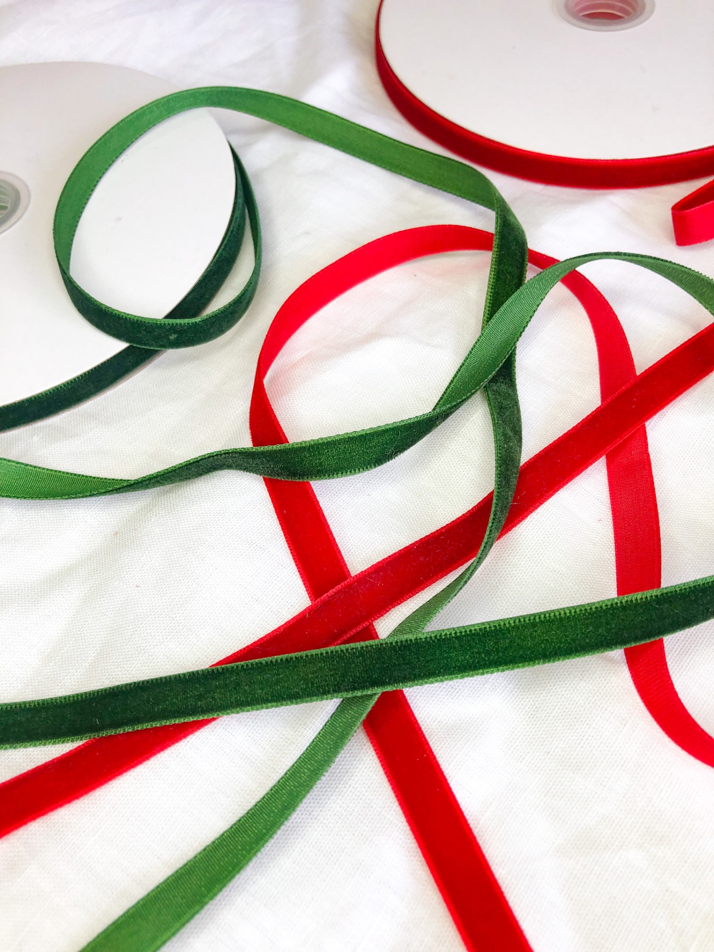 Fitas de veludo verde e vermelho com carretéis sobre pano branco