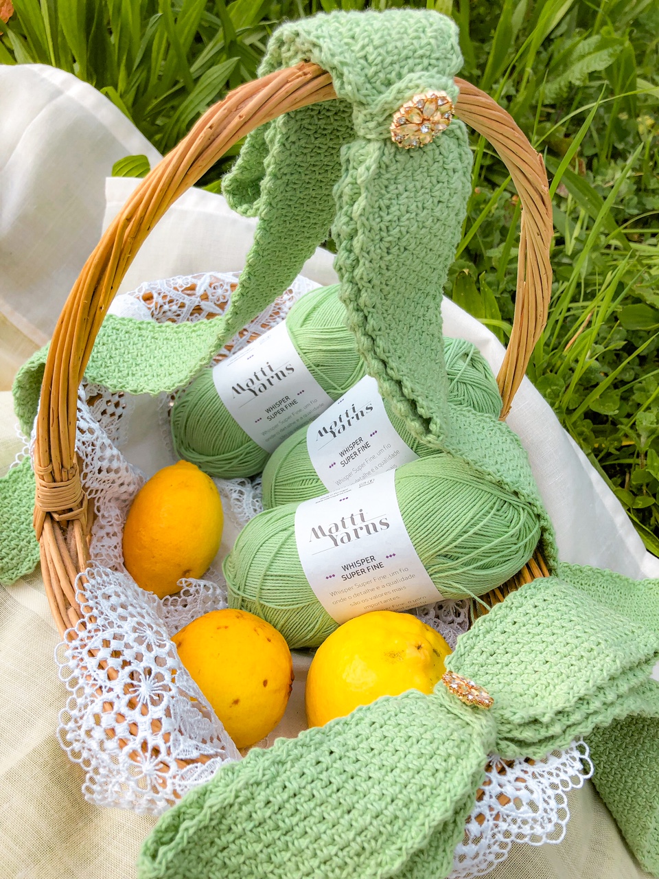 Cesto de vime com novelos de lã verde claro e limões amarelos decorados com fita de malha