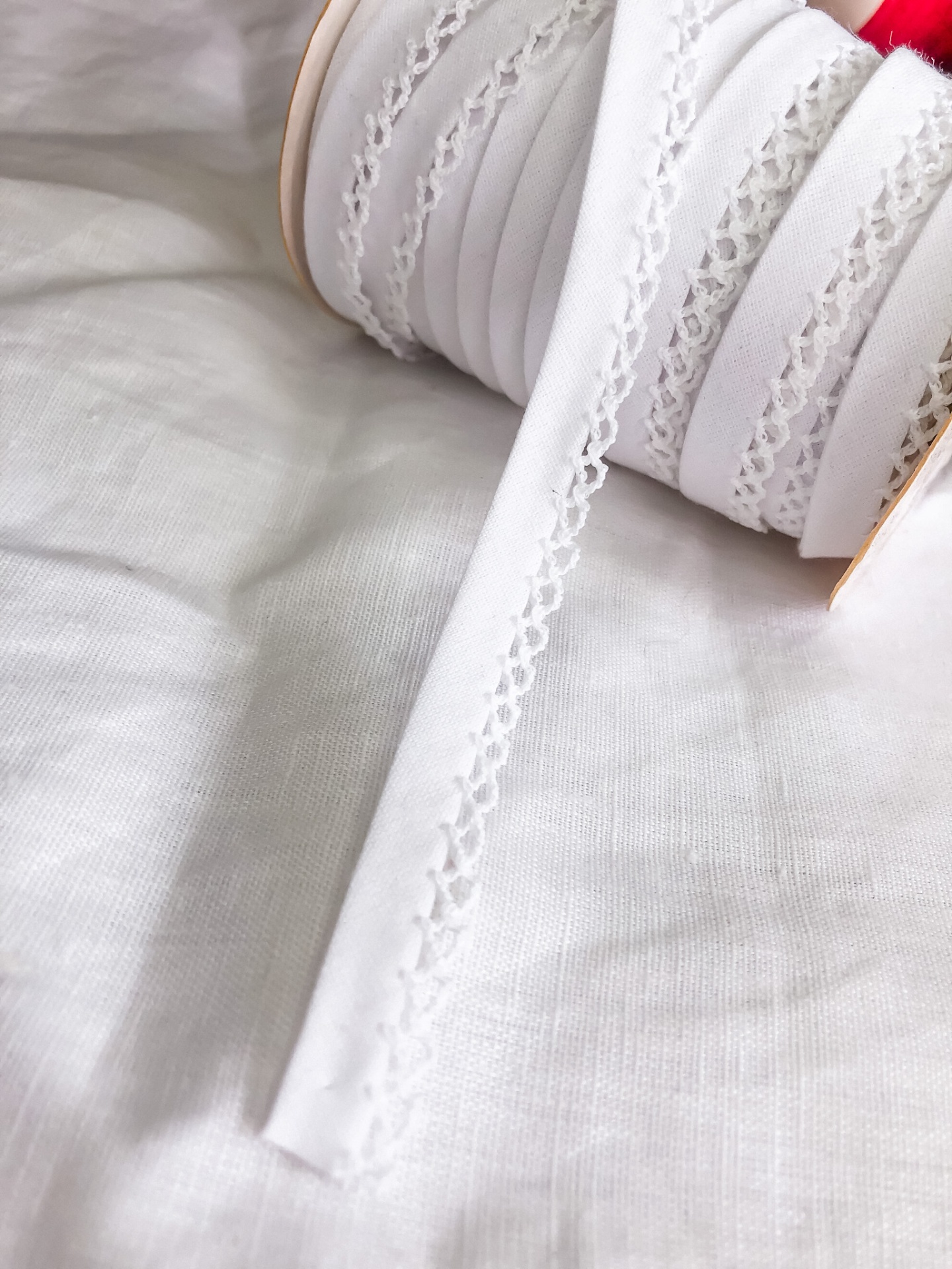Fita branca decorativa em rolo sobre tecido branco.