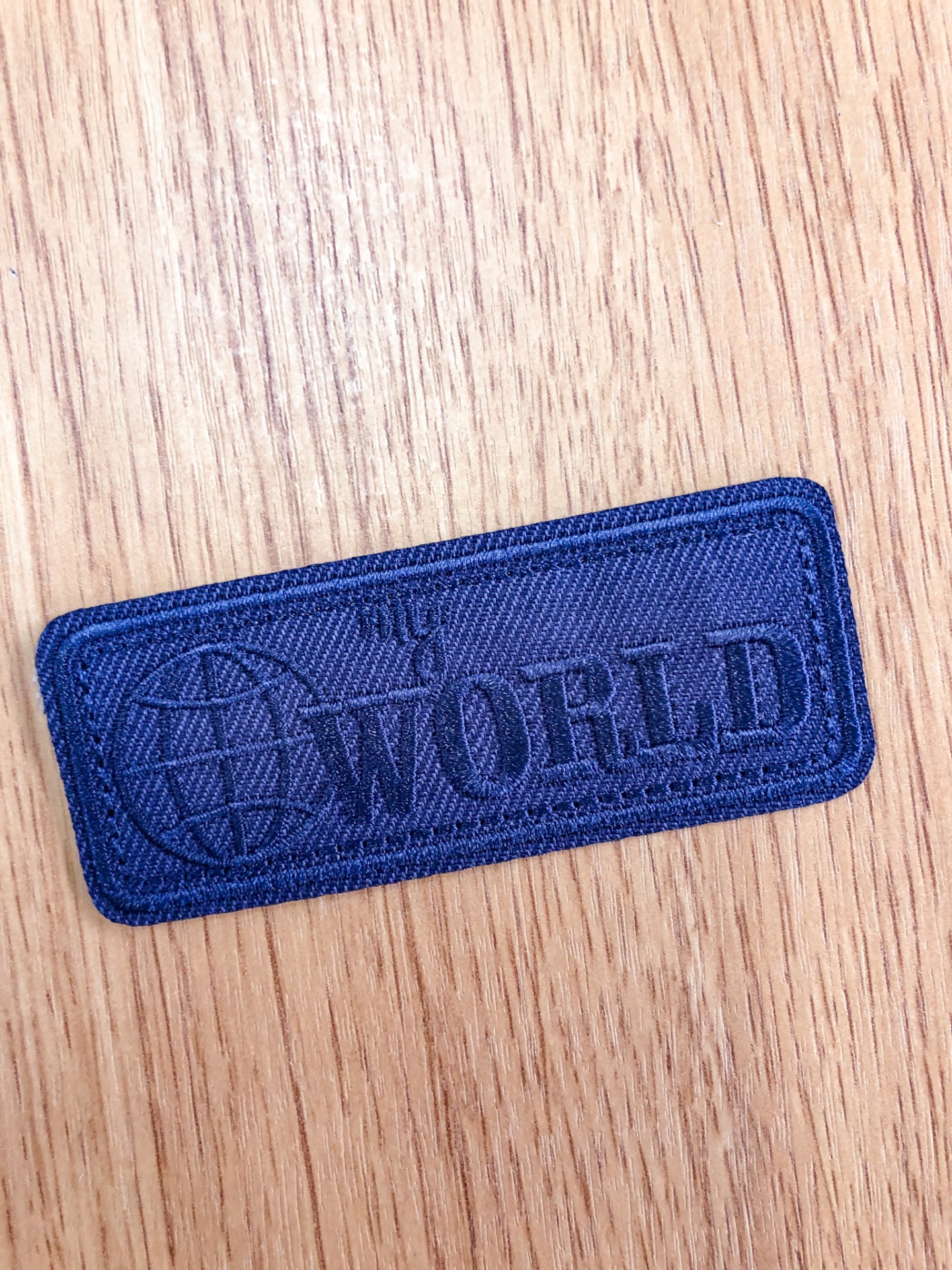 Etiqueta em tecido azul escuro com texto em relevo WORLD e globo