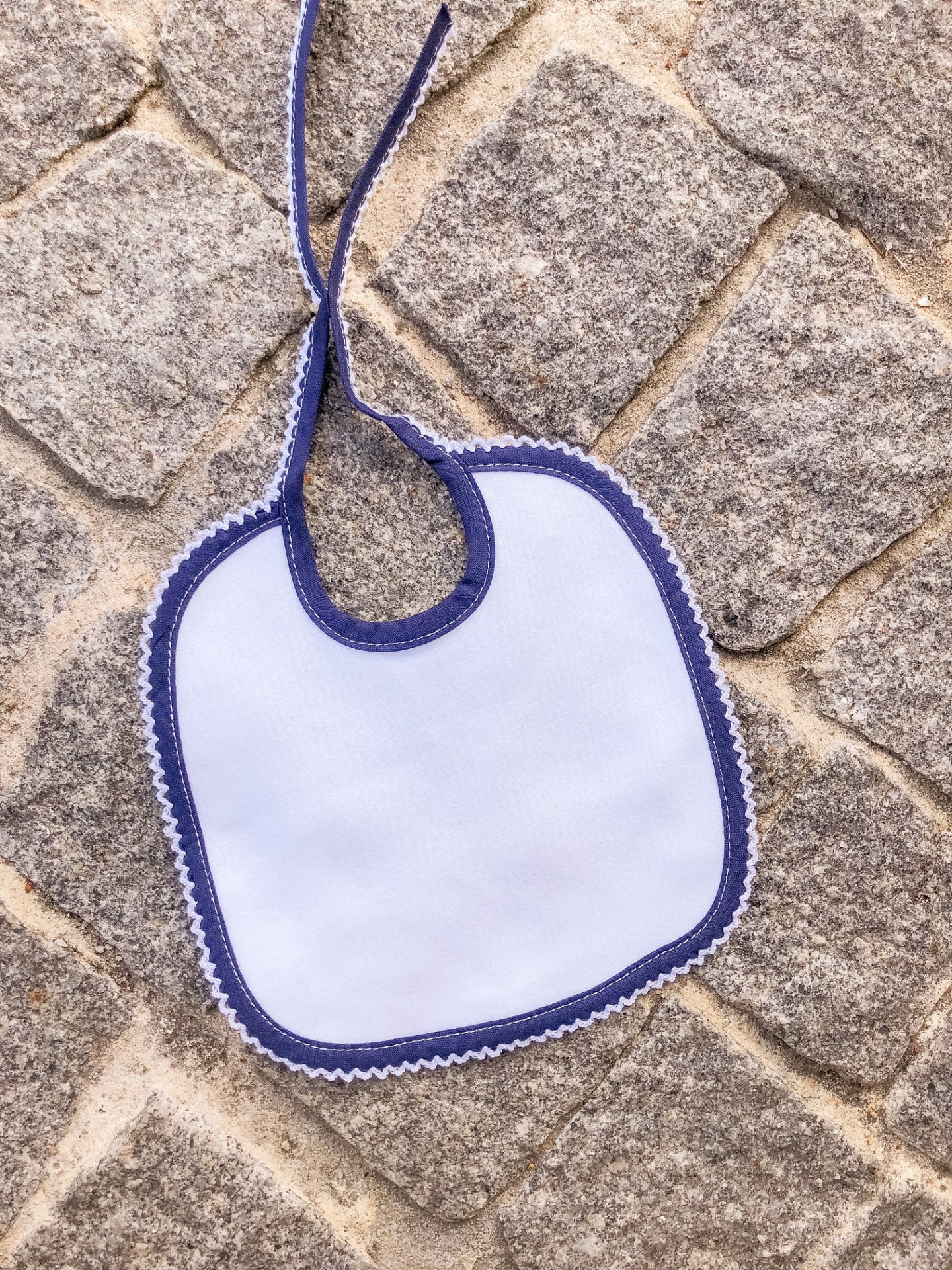 Babete de bebé branco com contorno azul numa calçada de pedra