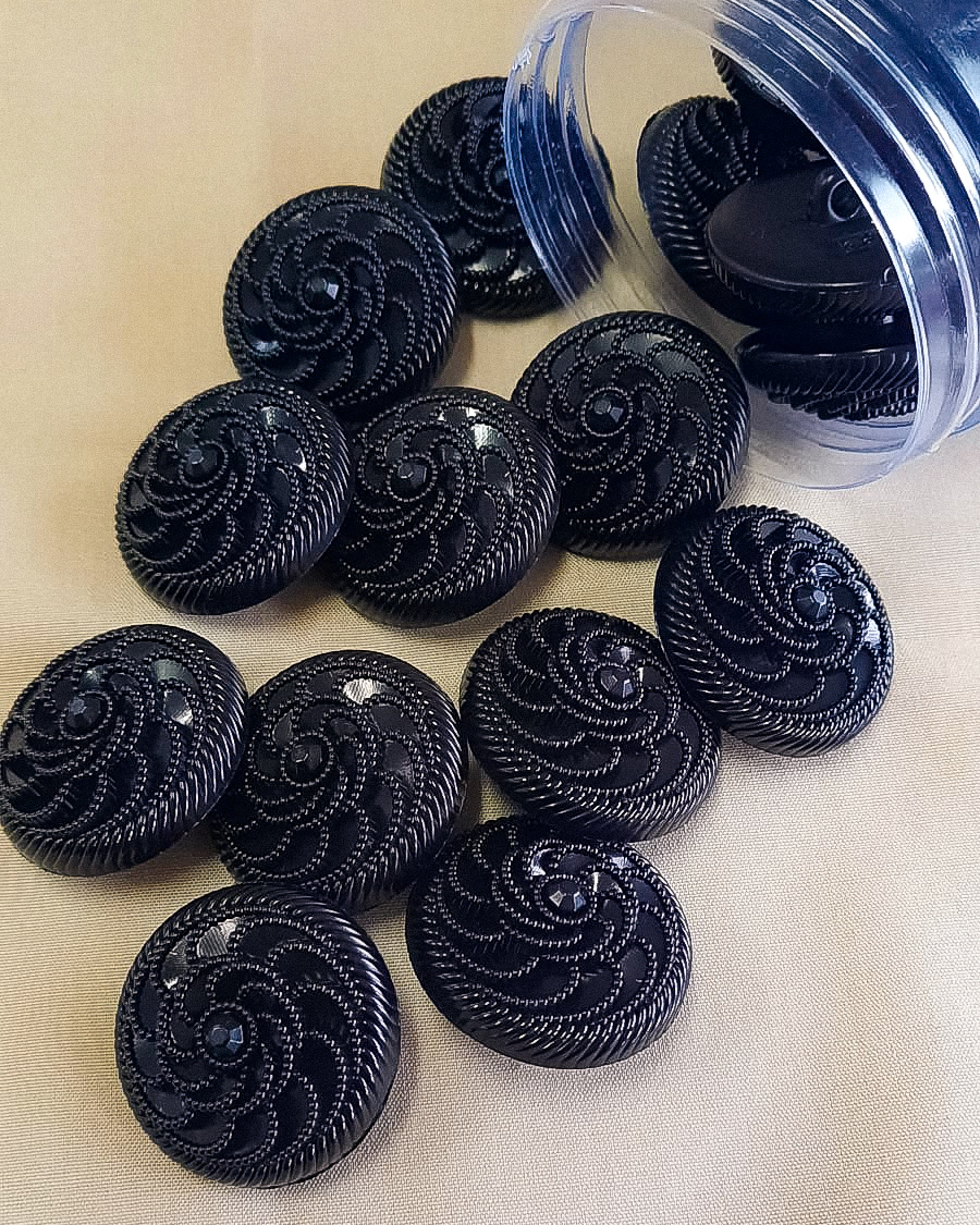 Botões pretos com padrão em espiral e brilho em recipiente plástico