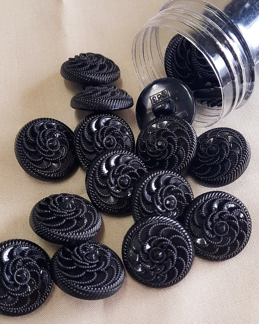 Botões pretos texturizados em espiral sobre superfície bege com recipiente plástico