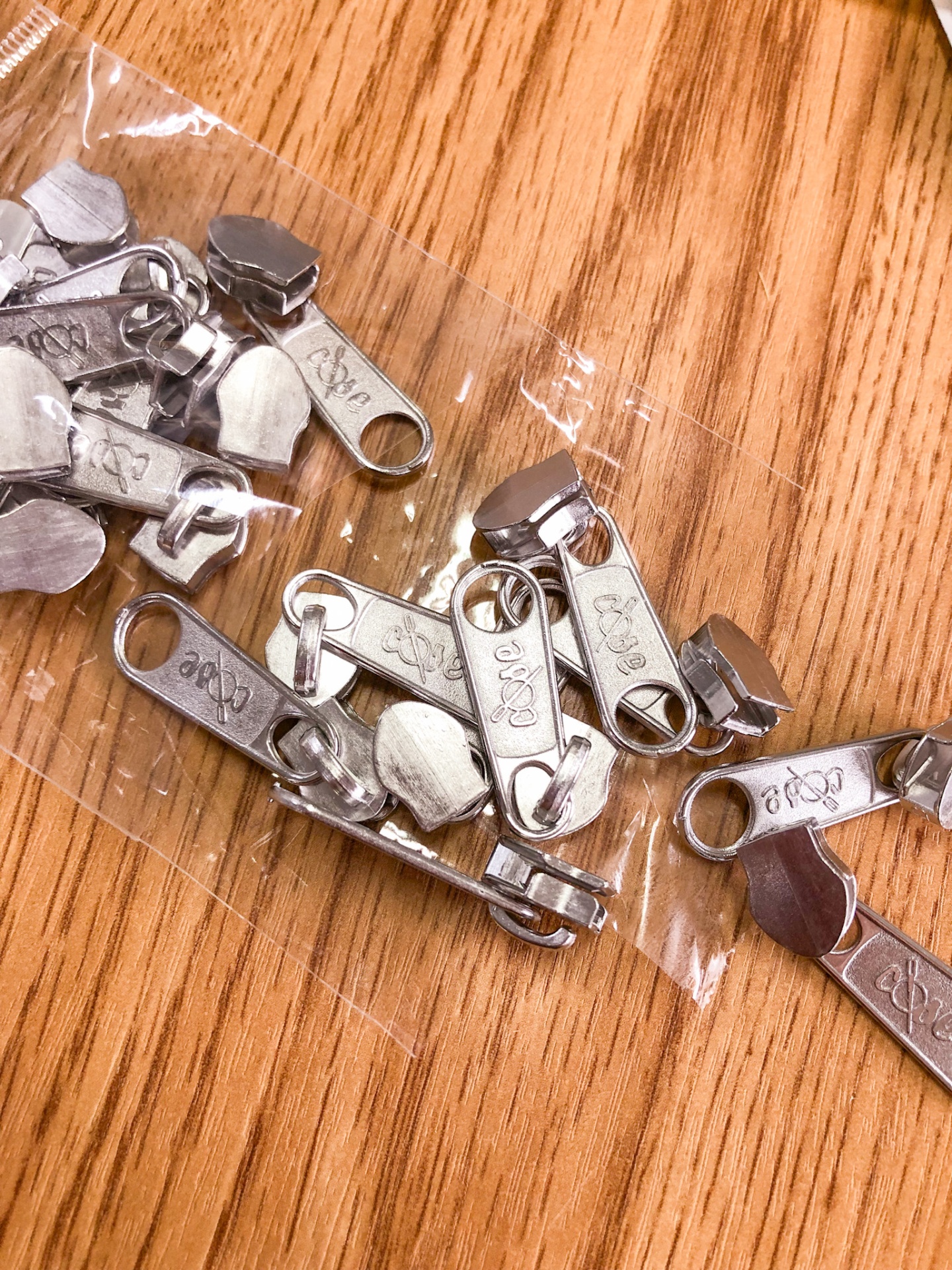 Puxadores metálicos prata para zíper em saco plástico sobre madeira