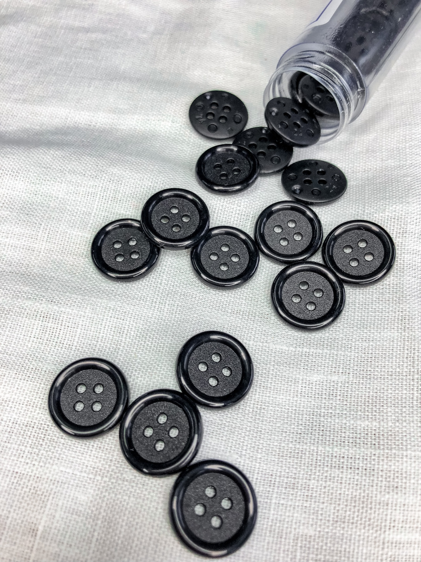 Botões pretos de quatro orifícios sobre tecido claro com recipiente transparente aberto