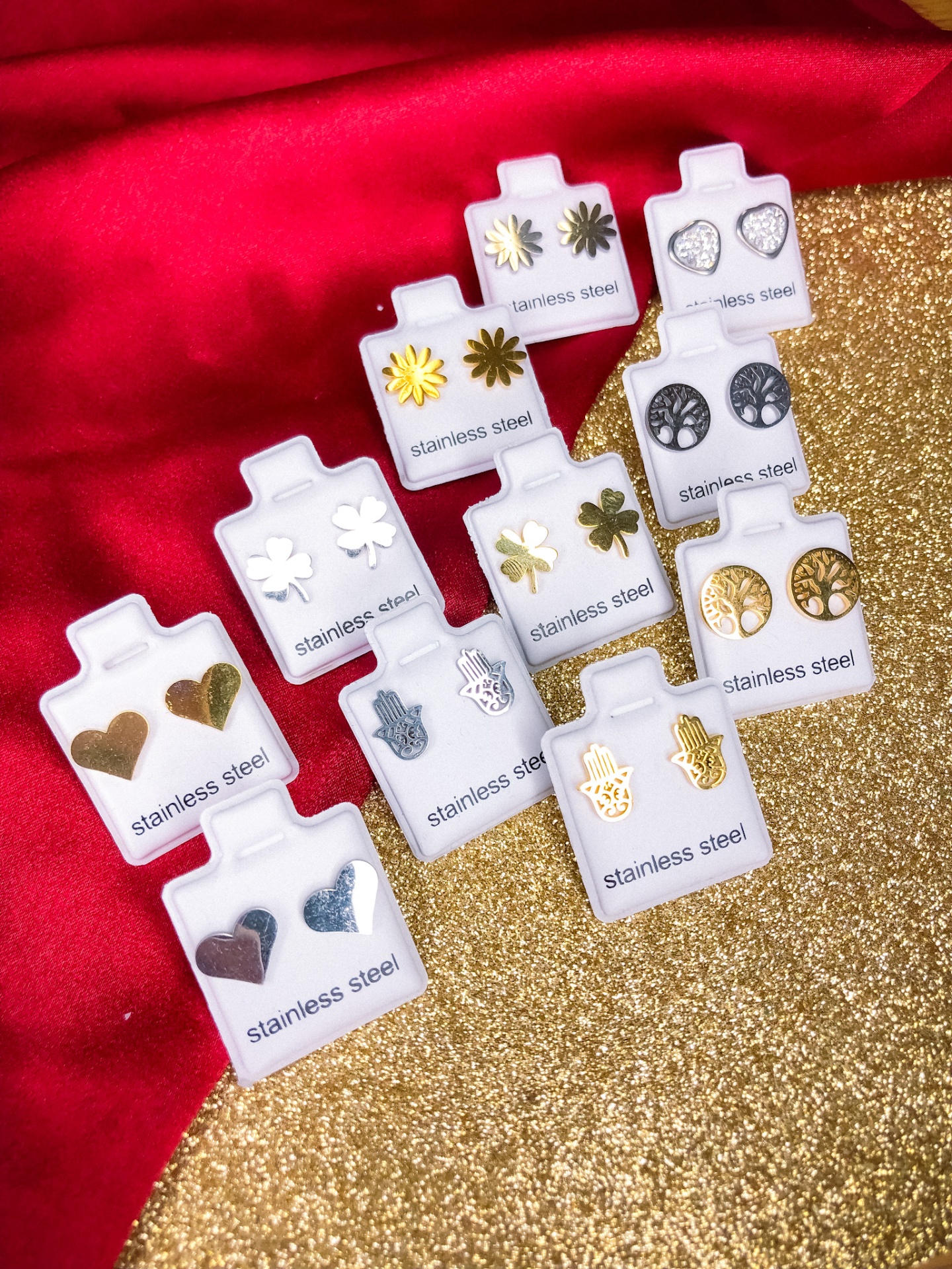 10 pares de brincos de aço inoxidável em suportes brancos sobre fundo vermelho e dourado