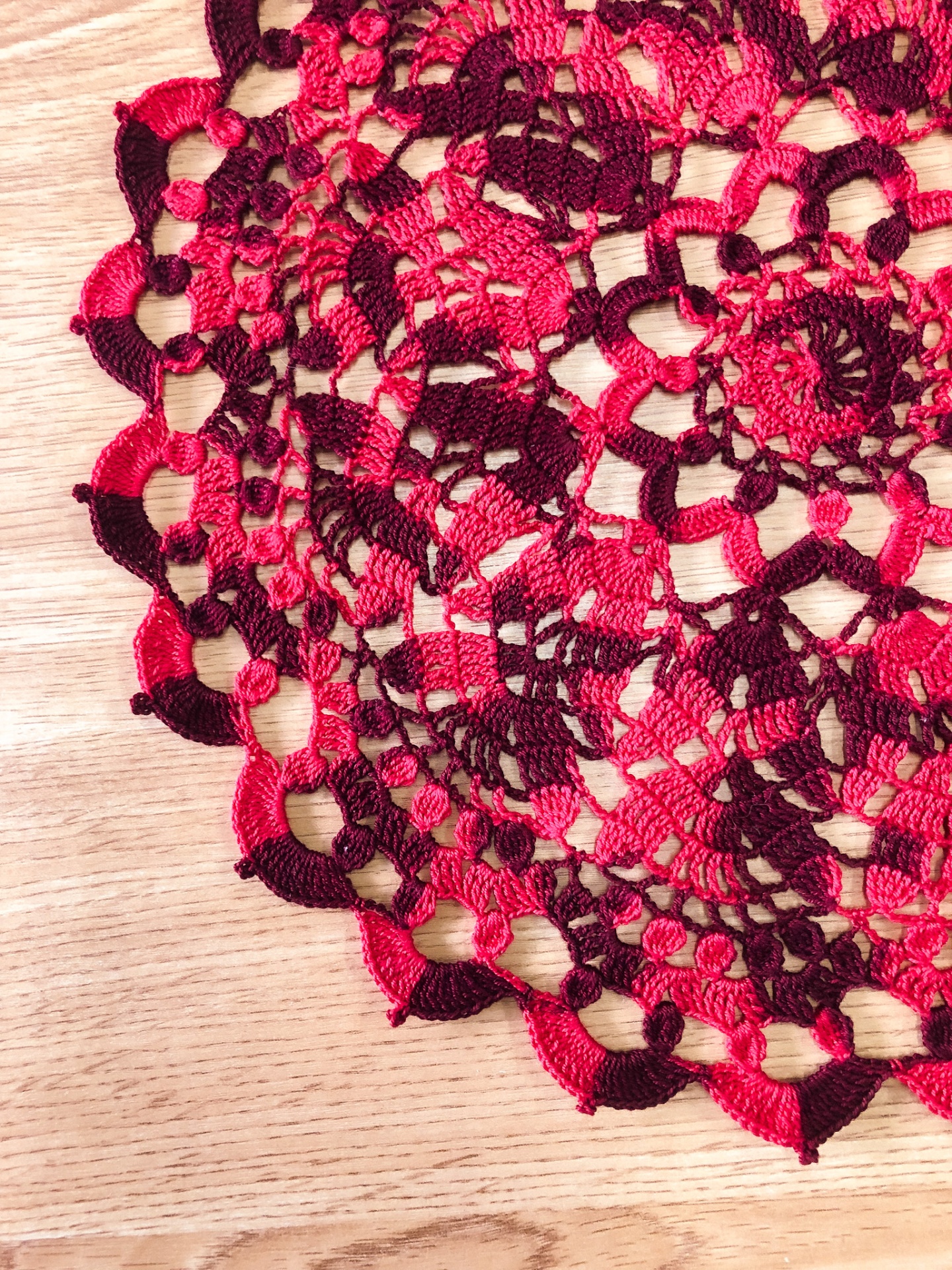 Toalha de mesa redonda em croché vermelho e castanho sobre madeira