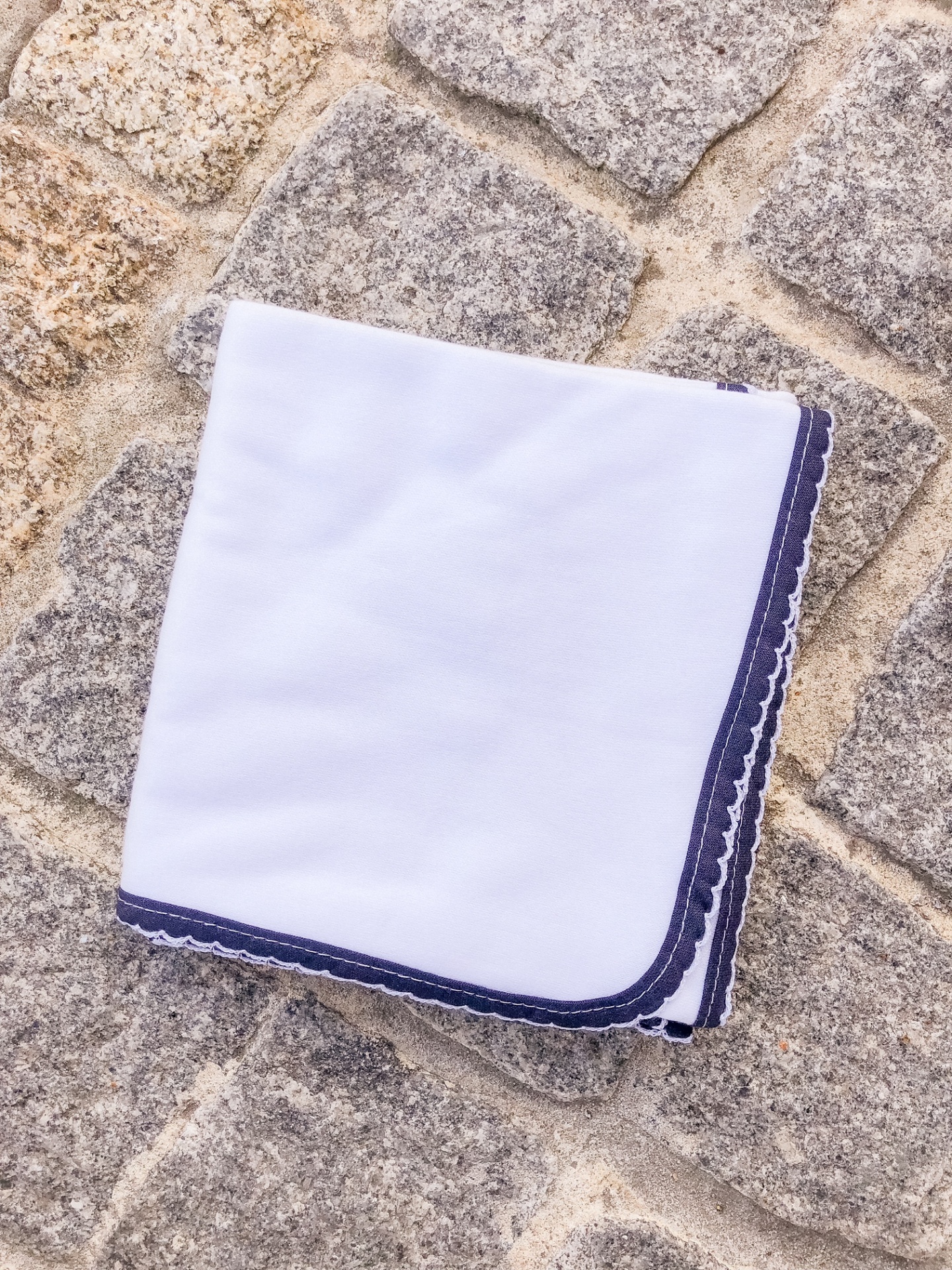 Lenço branco com borda azul sobre pavimento de pedra
