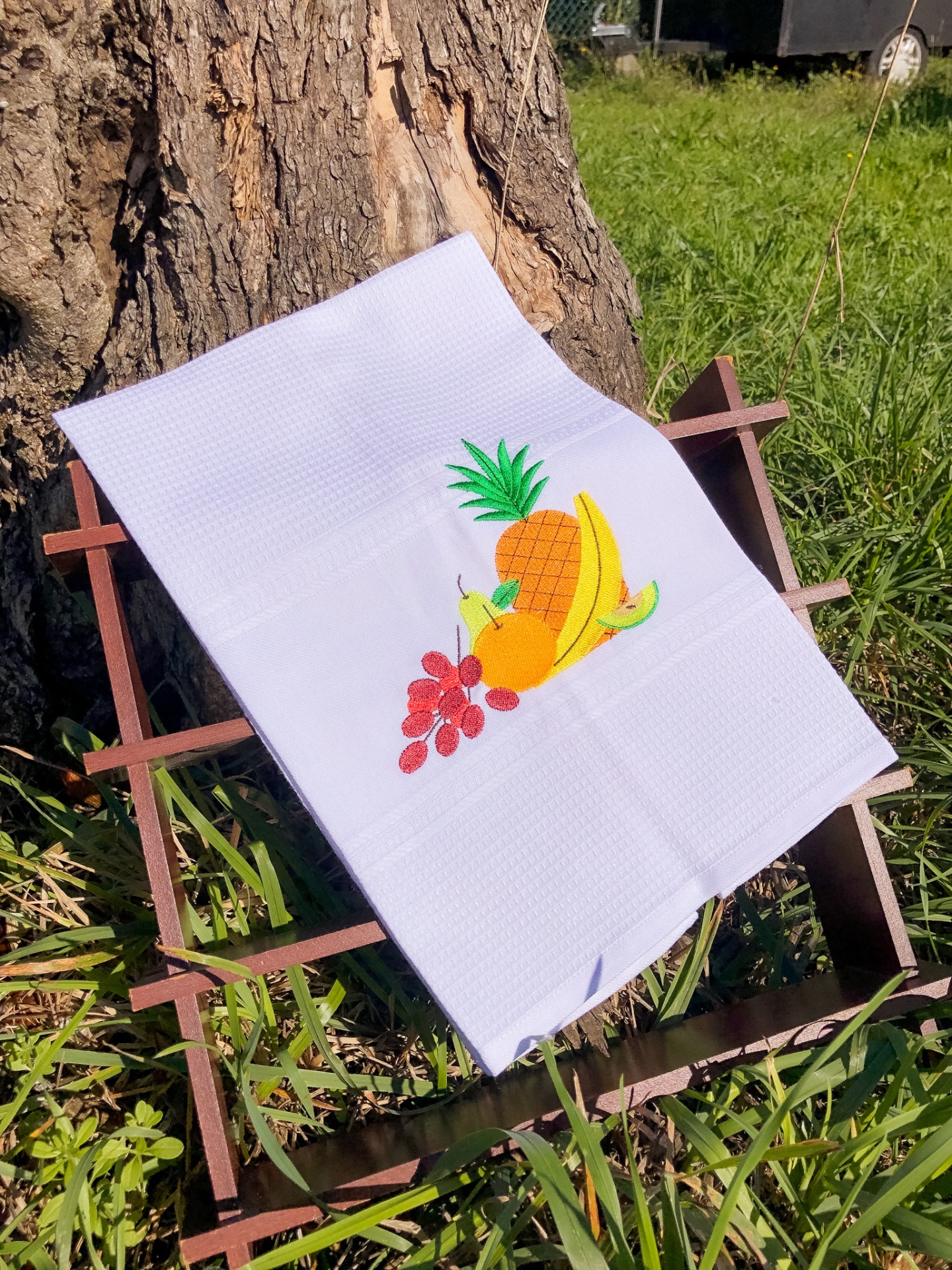 Toalha branca com bordado de frutas sobre armação de madeira, ao ar livre