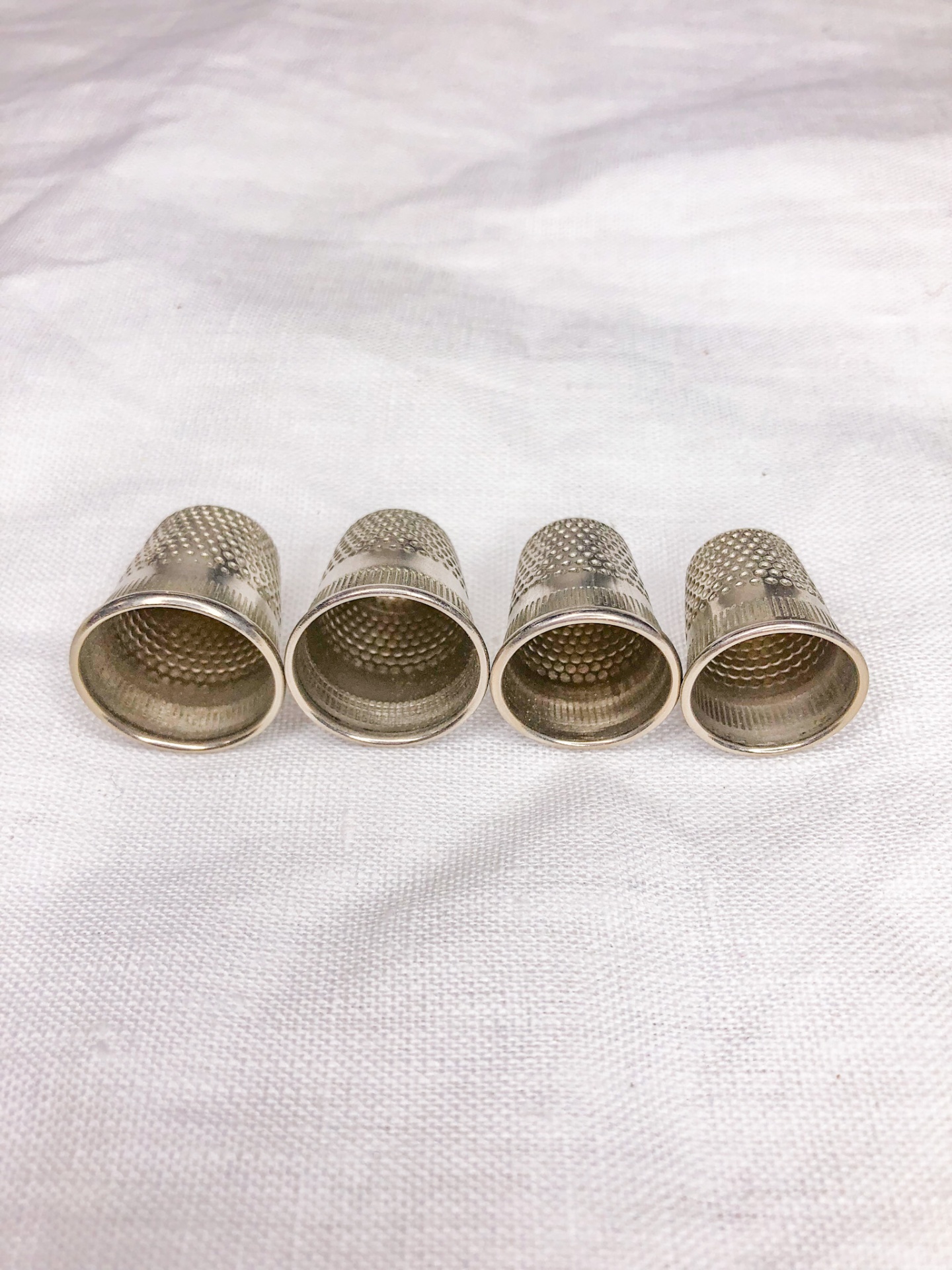Quatro dedais de metal prateado alinhados sobre tecido branco