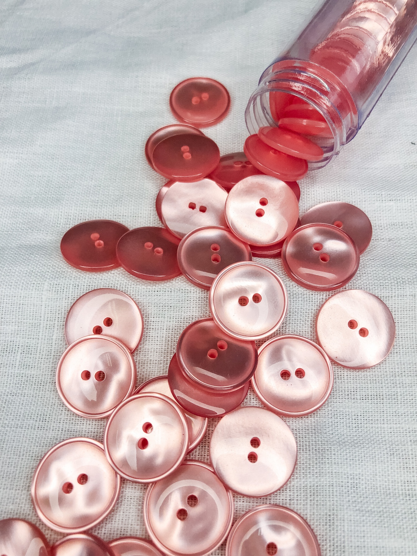 Botões de plástico rosa e vermelho em tecido branco com frasco plástico