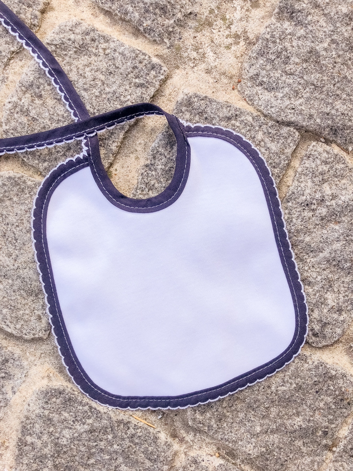 Babete branco com borda azul escuro sobre superfície de pedra