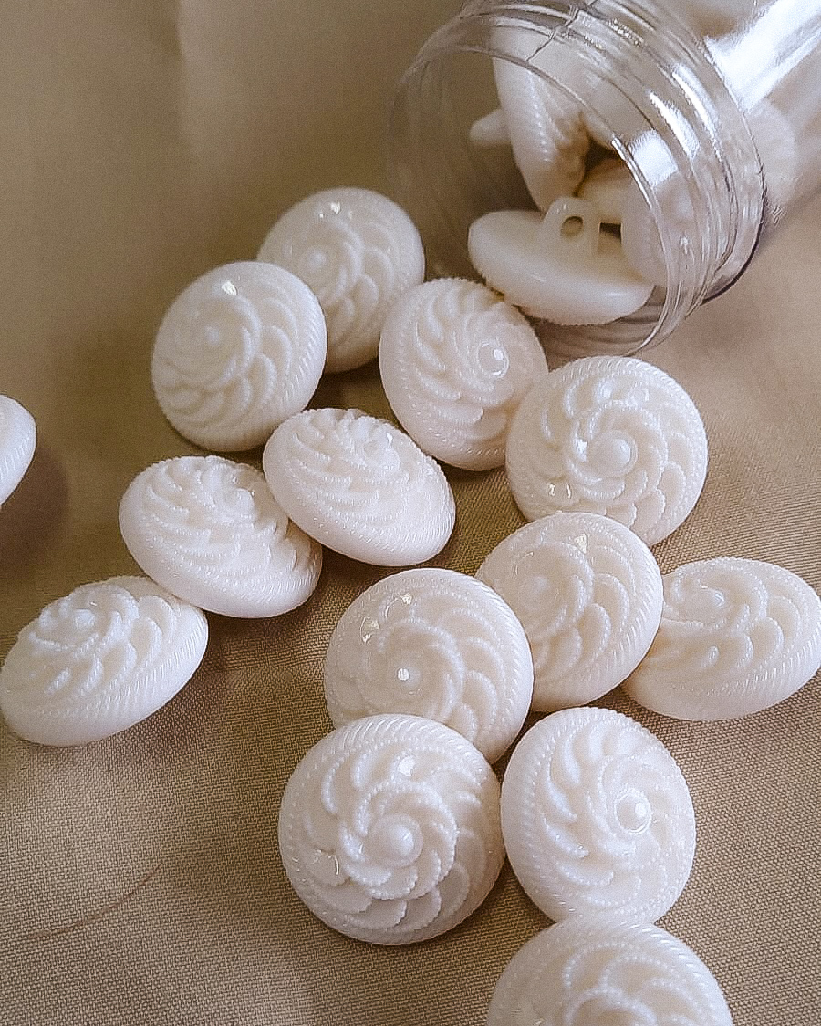 Botões brancos com padrão floral em relevo numa superfície bege