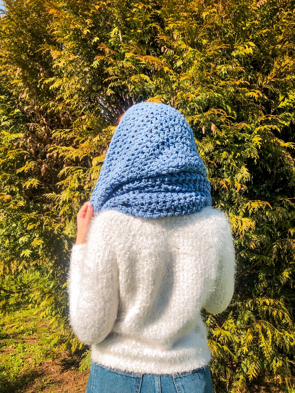 Pessoa de costas com camisola branca felpuda, jeans e cachecol azul claro ao ar livre