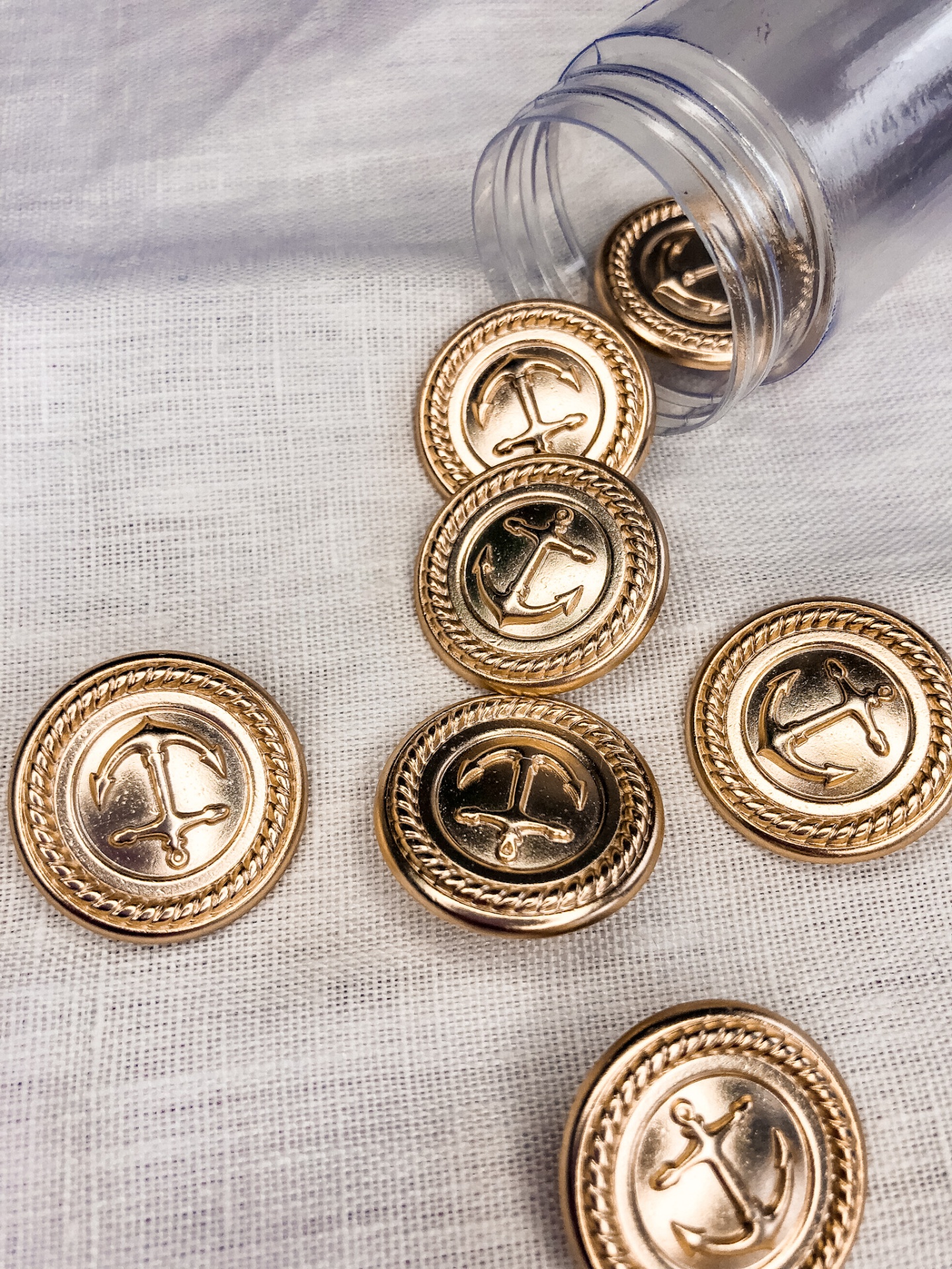 Botões dourados com âncora em frasco sobre tecido branco