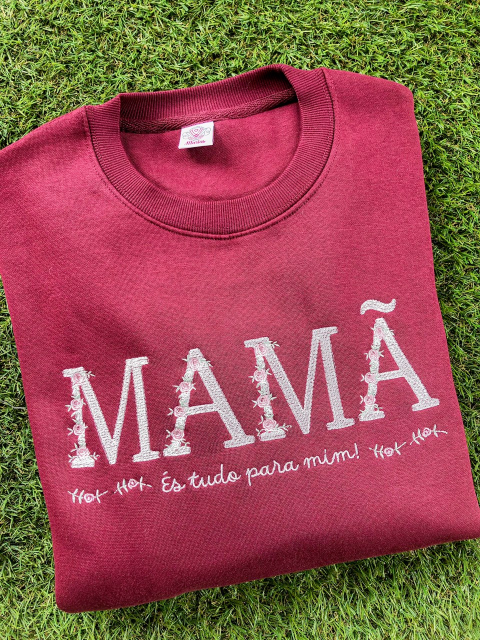 Sweatshirt bordô com texto bordado MAMÃ e frase em português sobre relvado.