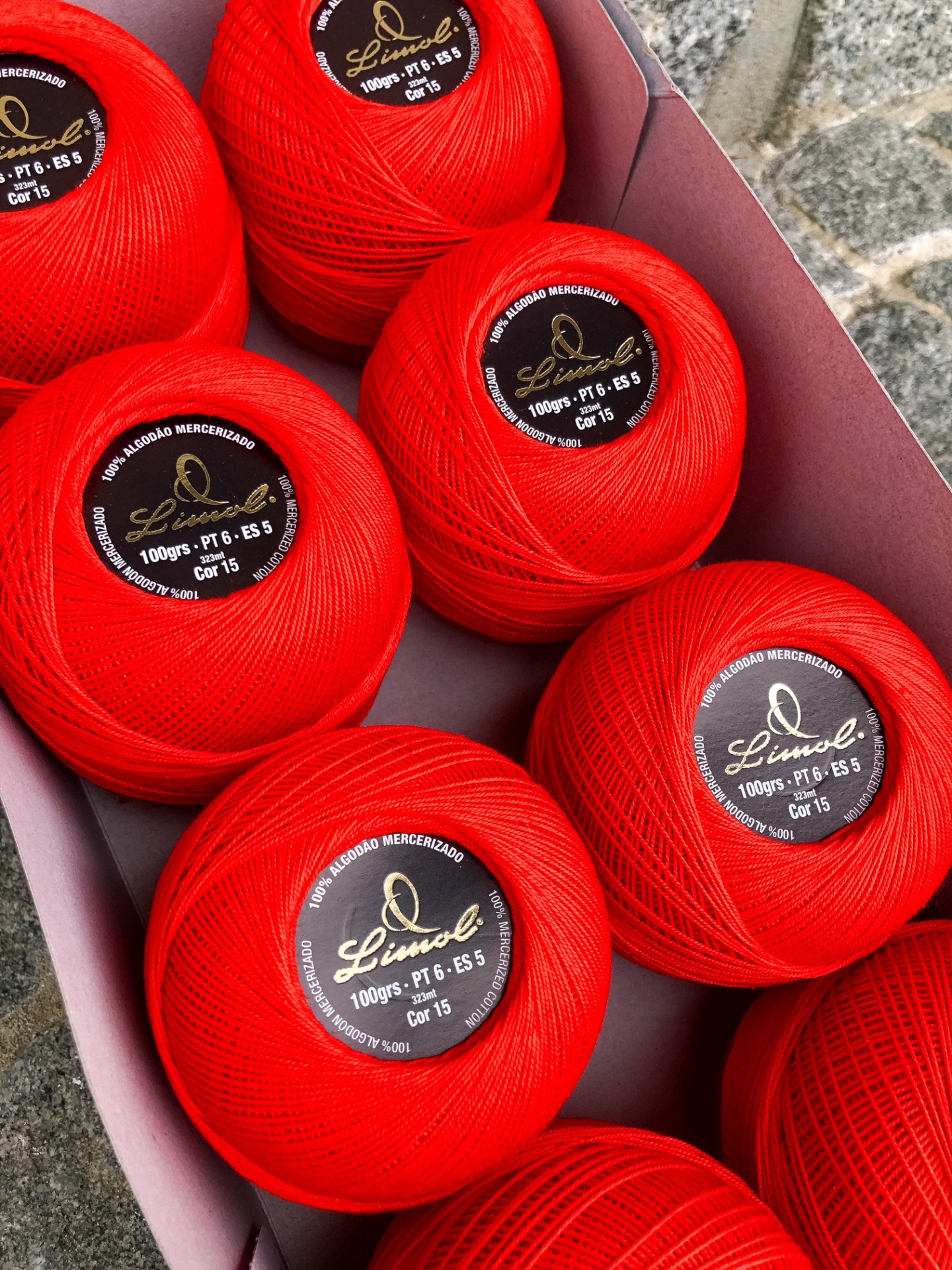 Novelos de fio vermelho Linhoel numa caixa rosa sobre cimento