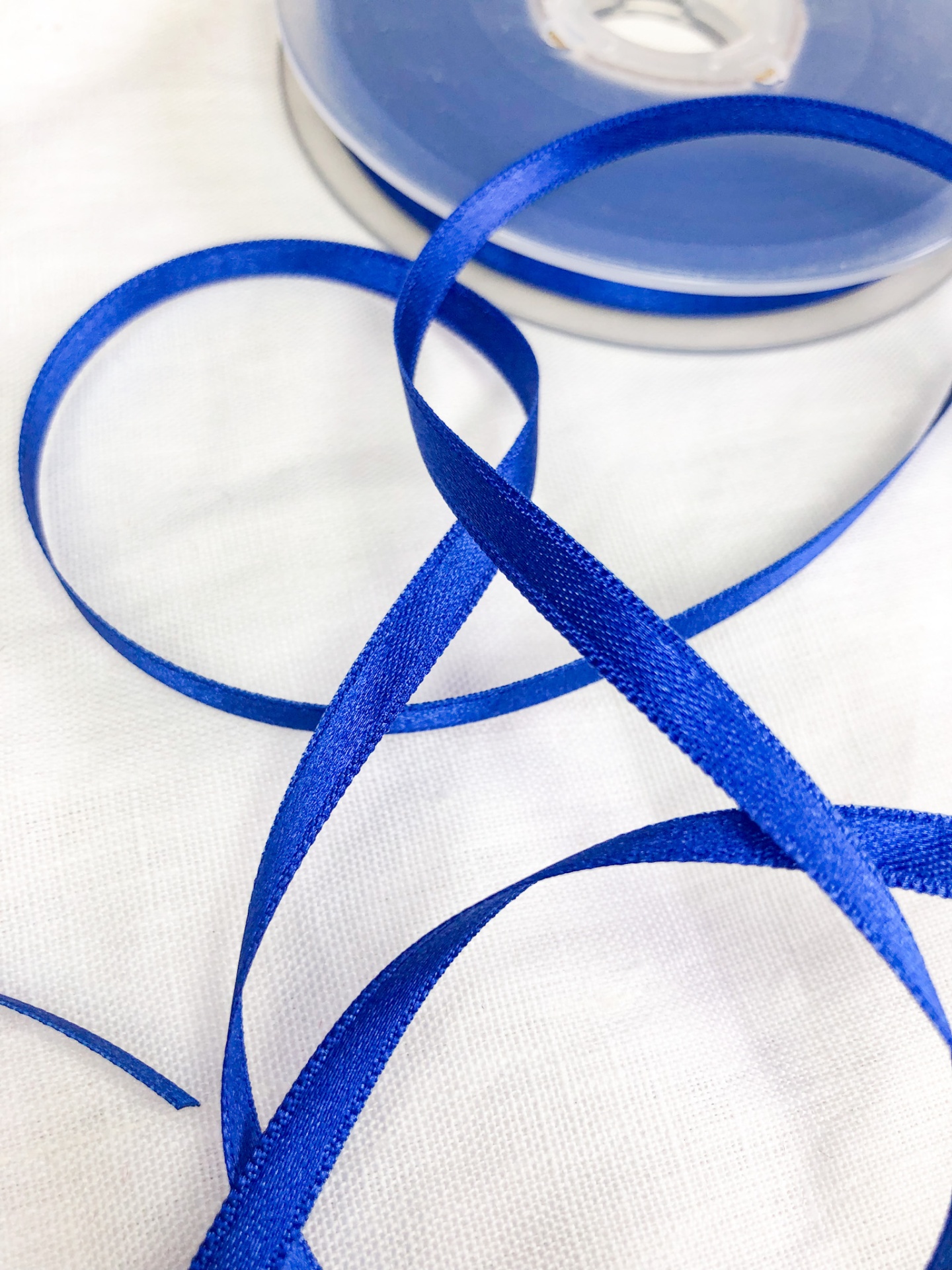 Fita de cetim azul royal numa bobina sobre tecido branco