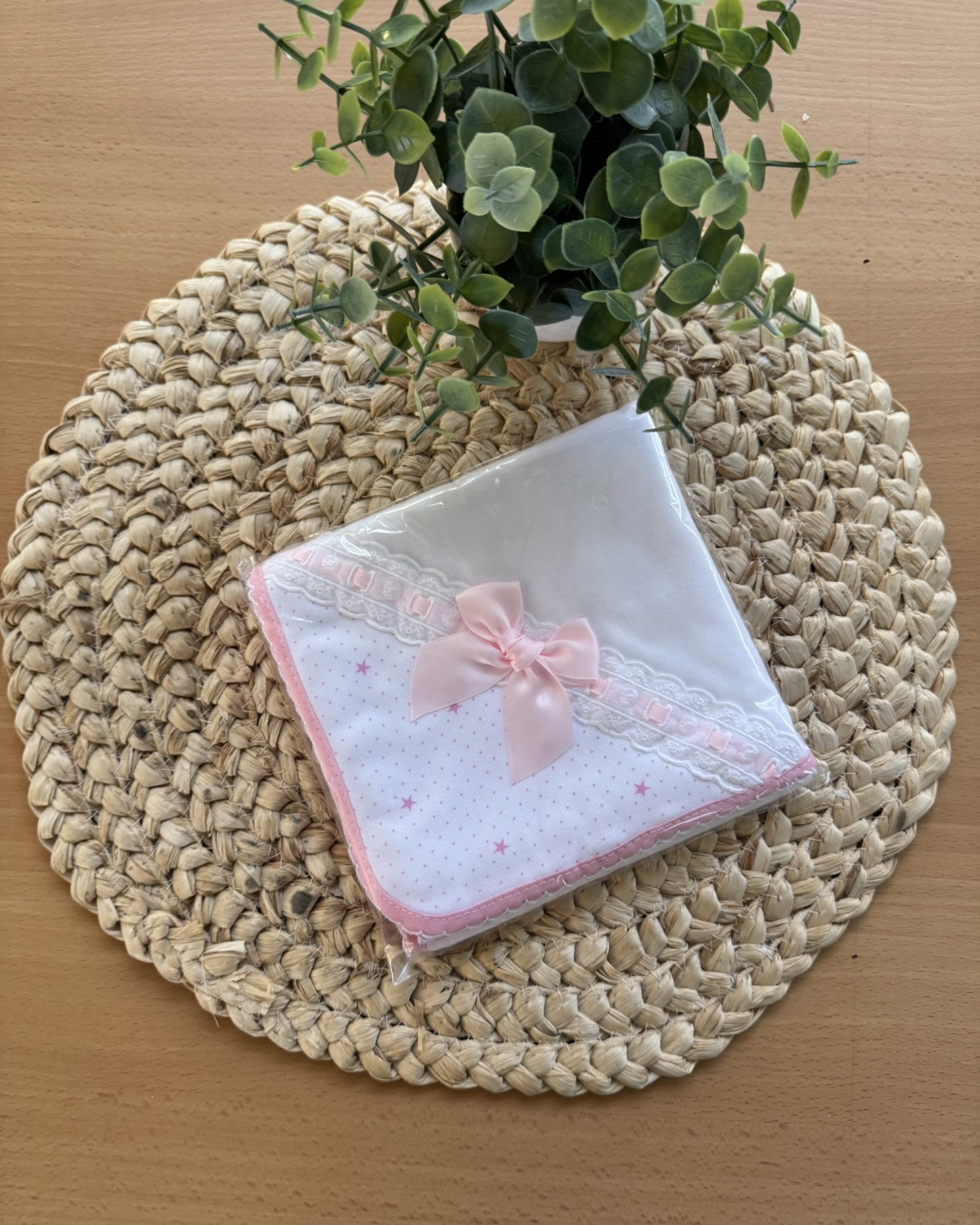 Fralda branca com laço rosa e renda sobre base de corda com planta verde