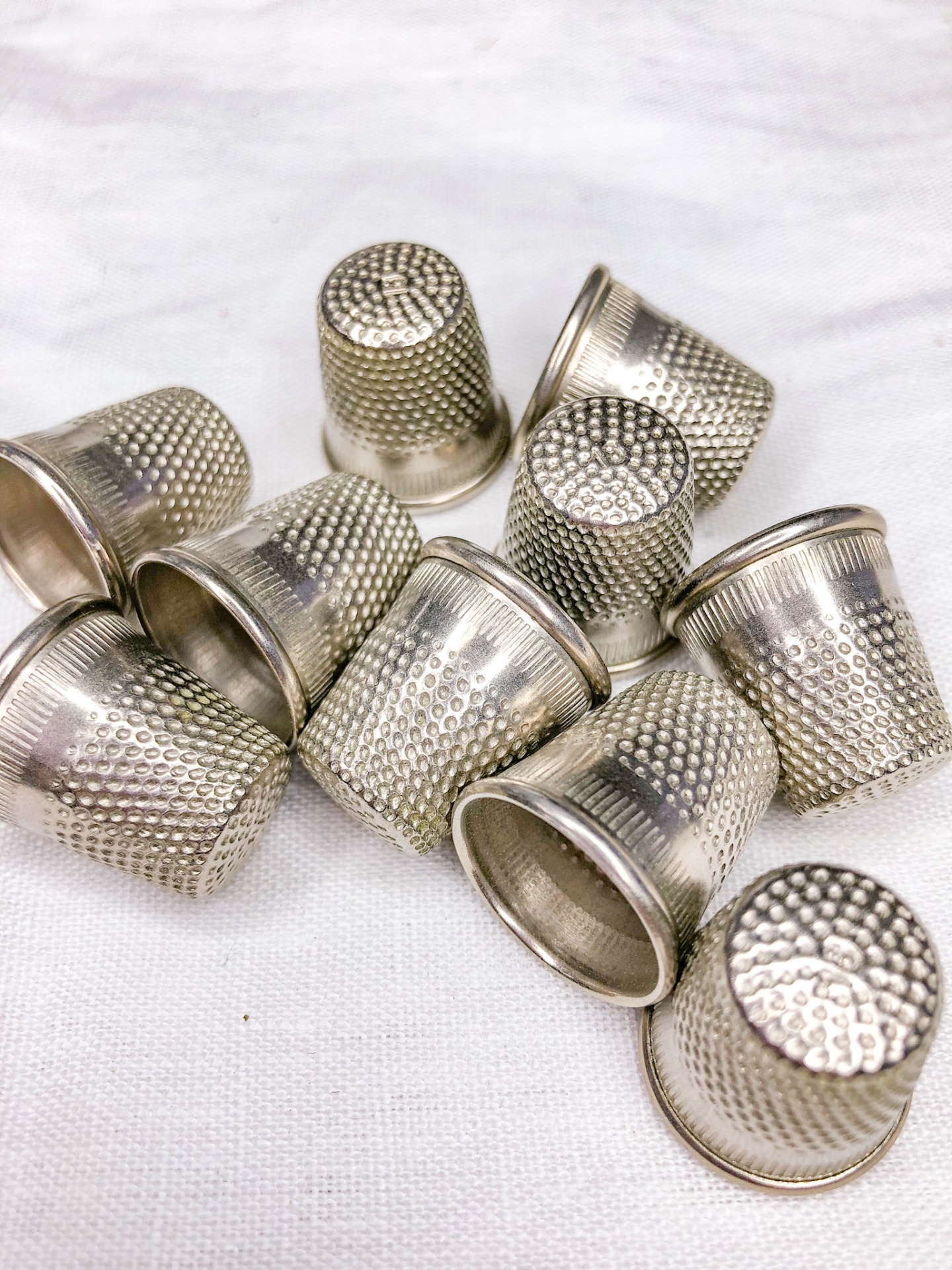 Dez dedais metálicos prateados com textura sobre tecido branco