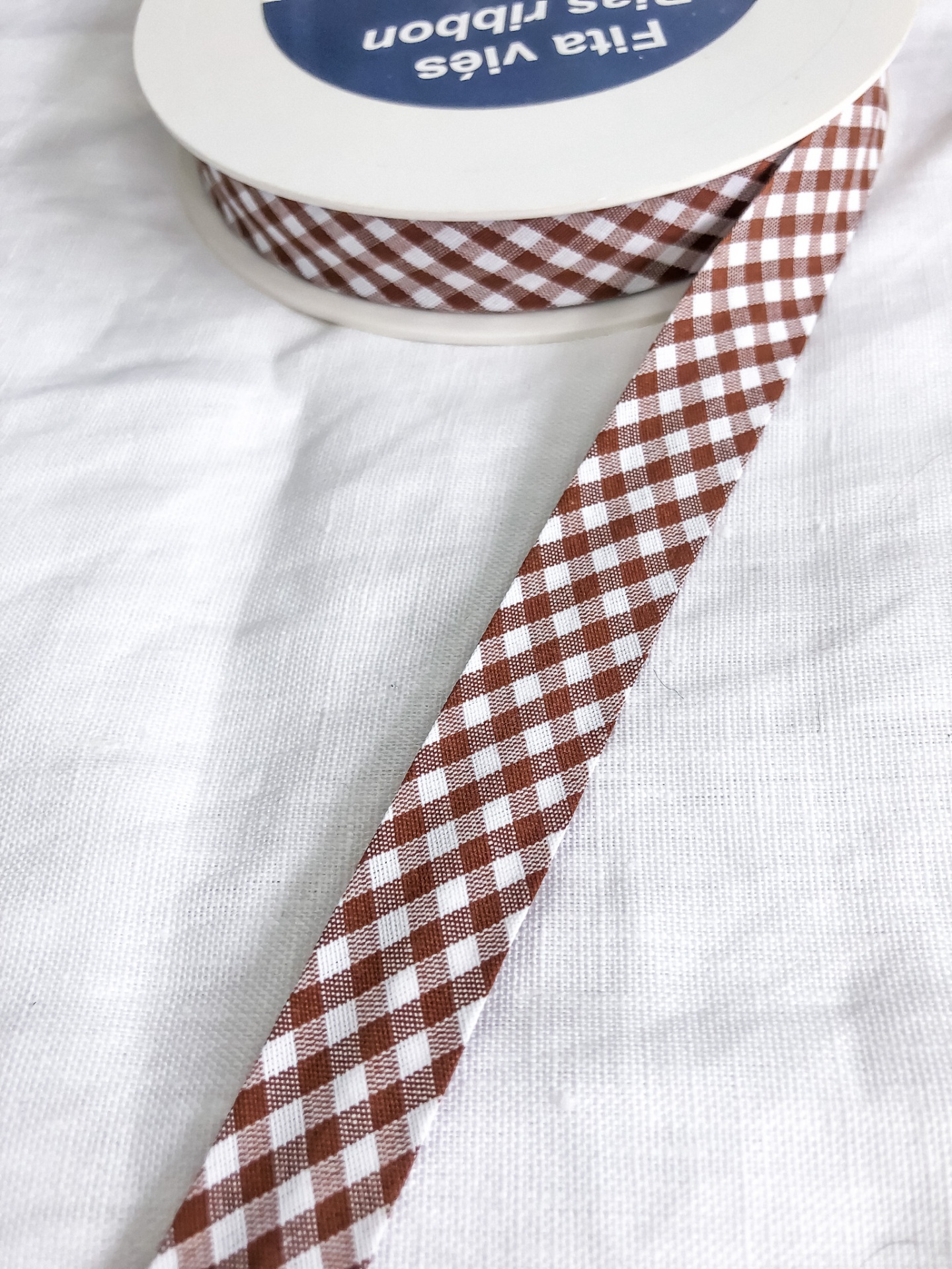 Fita de tecido xadrez castanha e branca em rolo com etiqueta azul