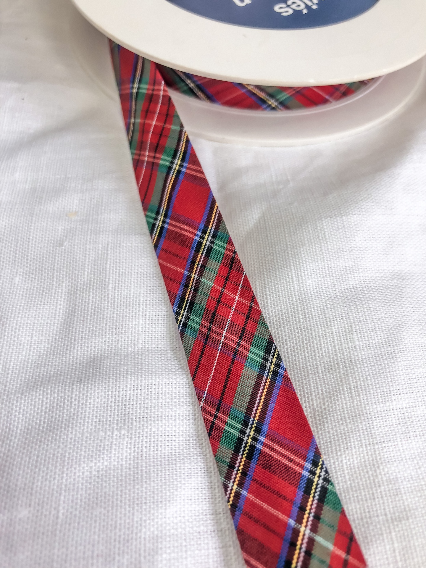 Fita xadrez colorida enrolada num carretel branco sobre tecido branco