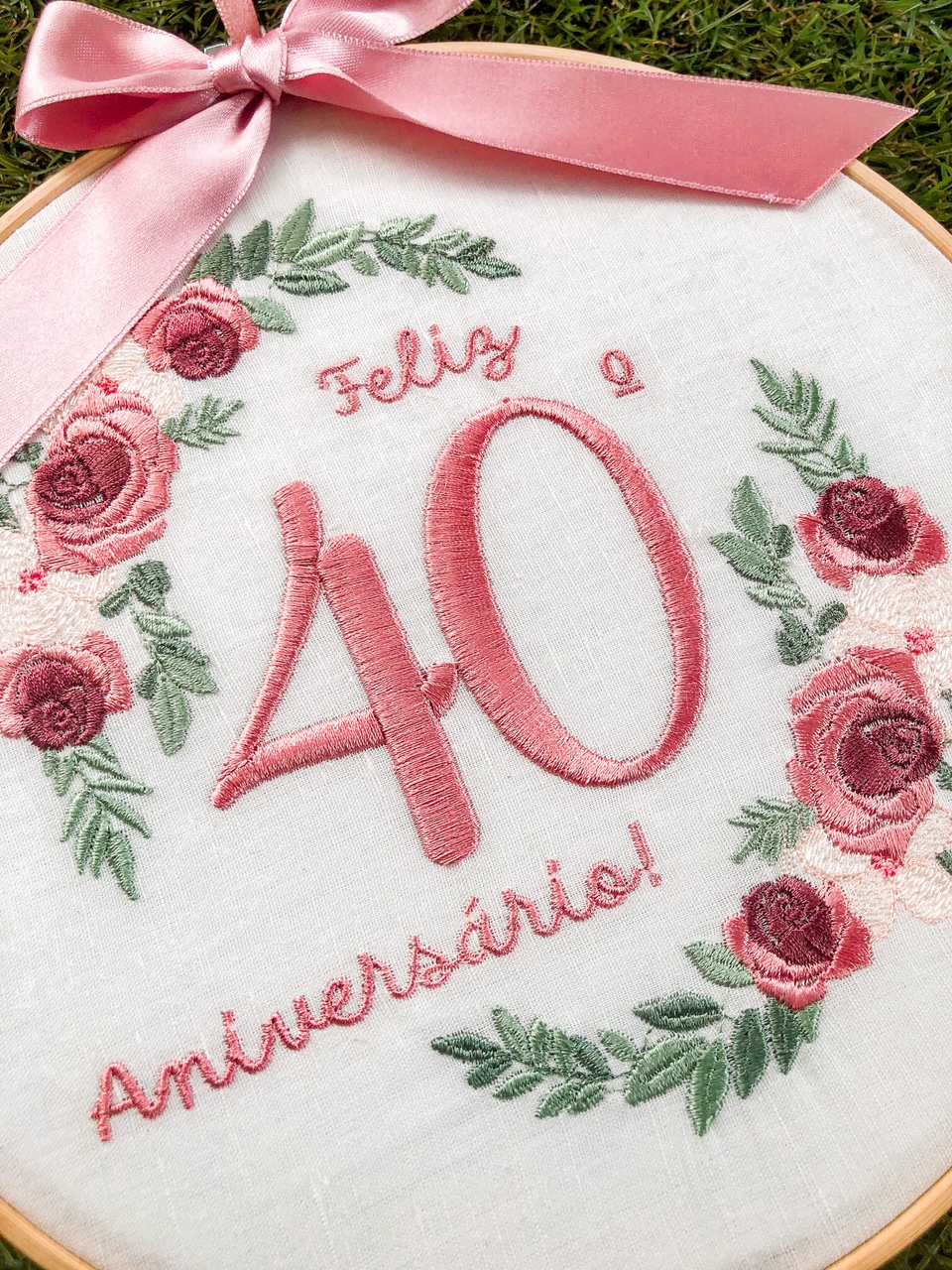 Bastidor bordado com flores rosas e texto Feliz 40 Aniversário em tecido branco com fita rosa.